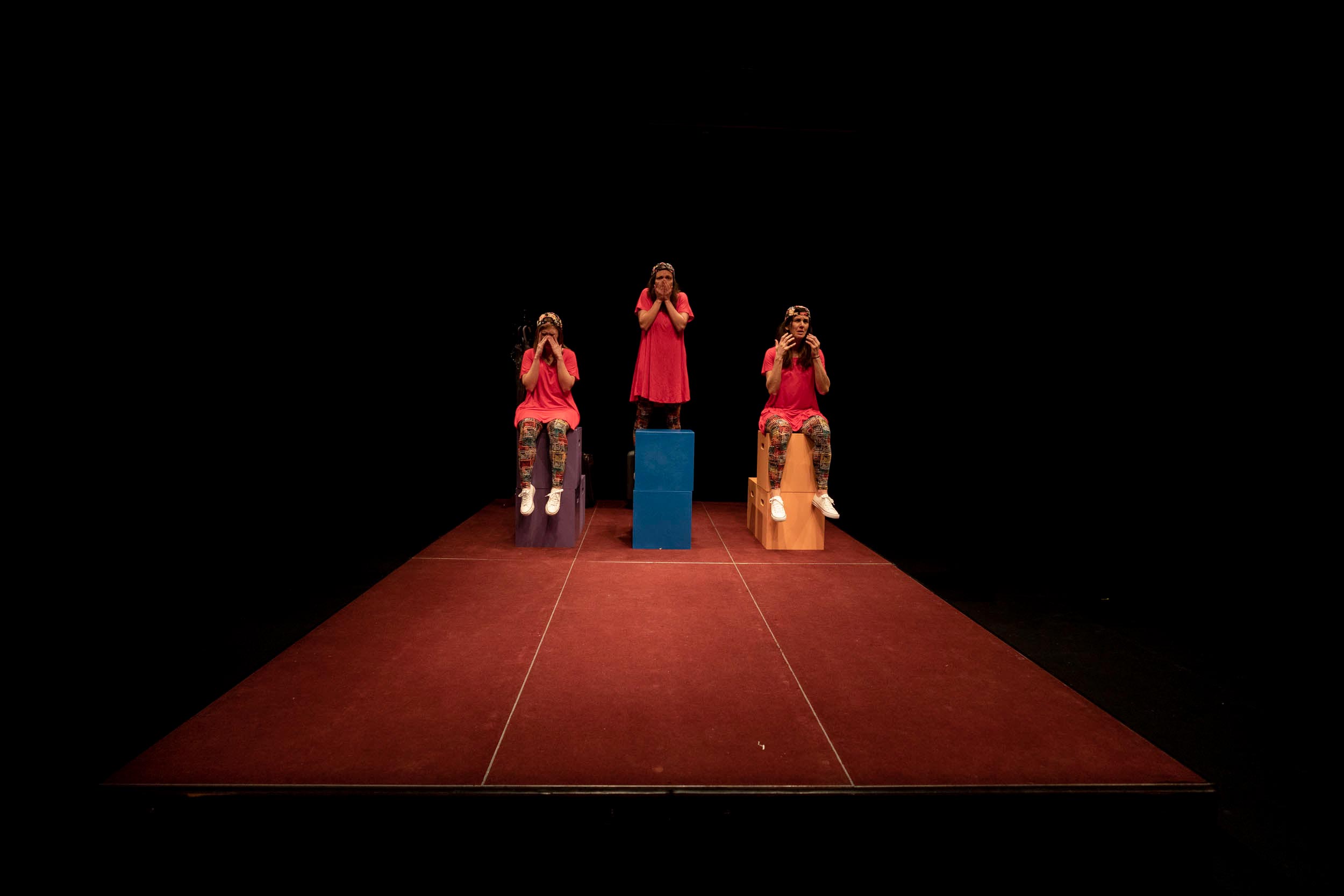 Left to right, Sarah Rabke, Melissa Frost and Alicia Lopez Operé sit on multicolored boxes in the spotlight