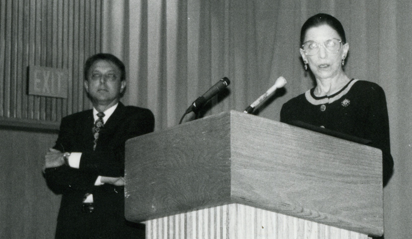 Robert Scott looks on as Ginsburg delivers the lecture at a podium