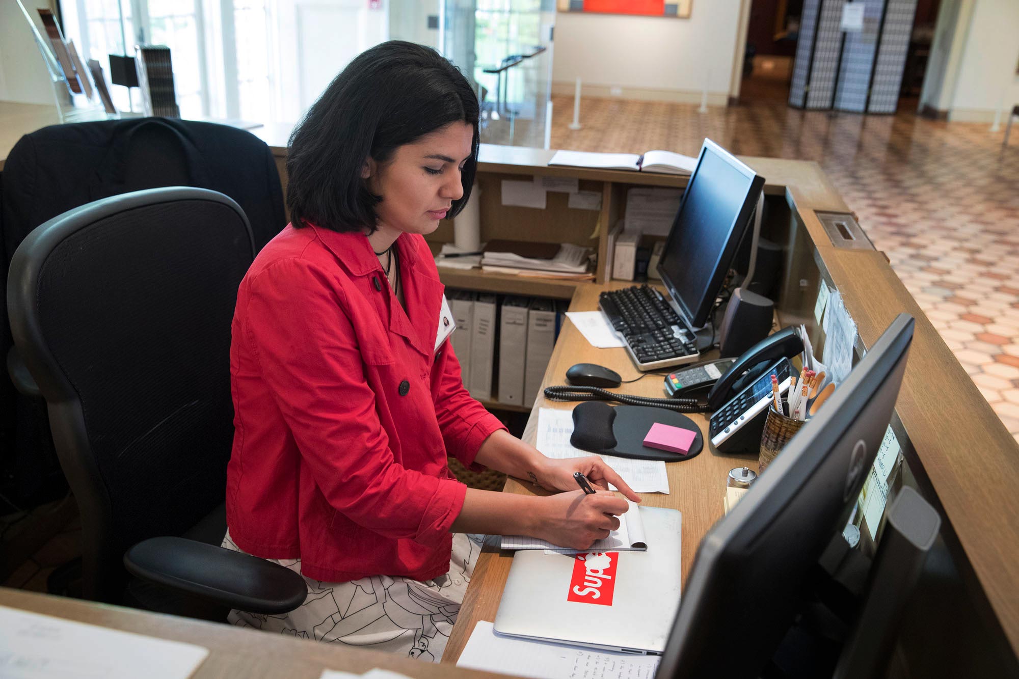 Haghtalab writes in a notepad at a receptionist desk 