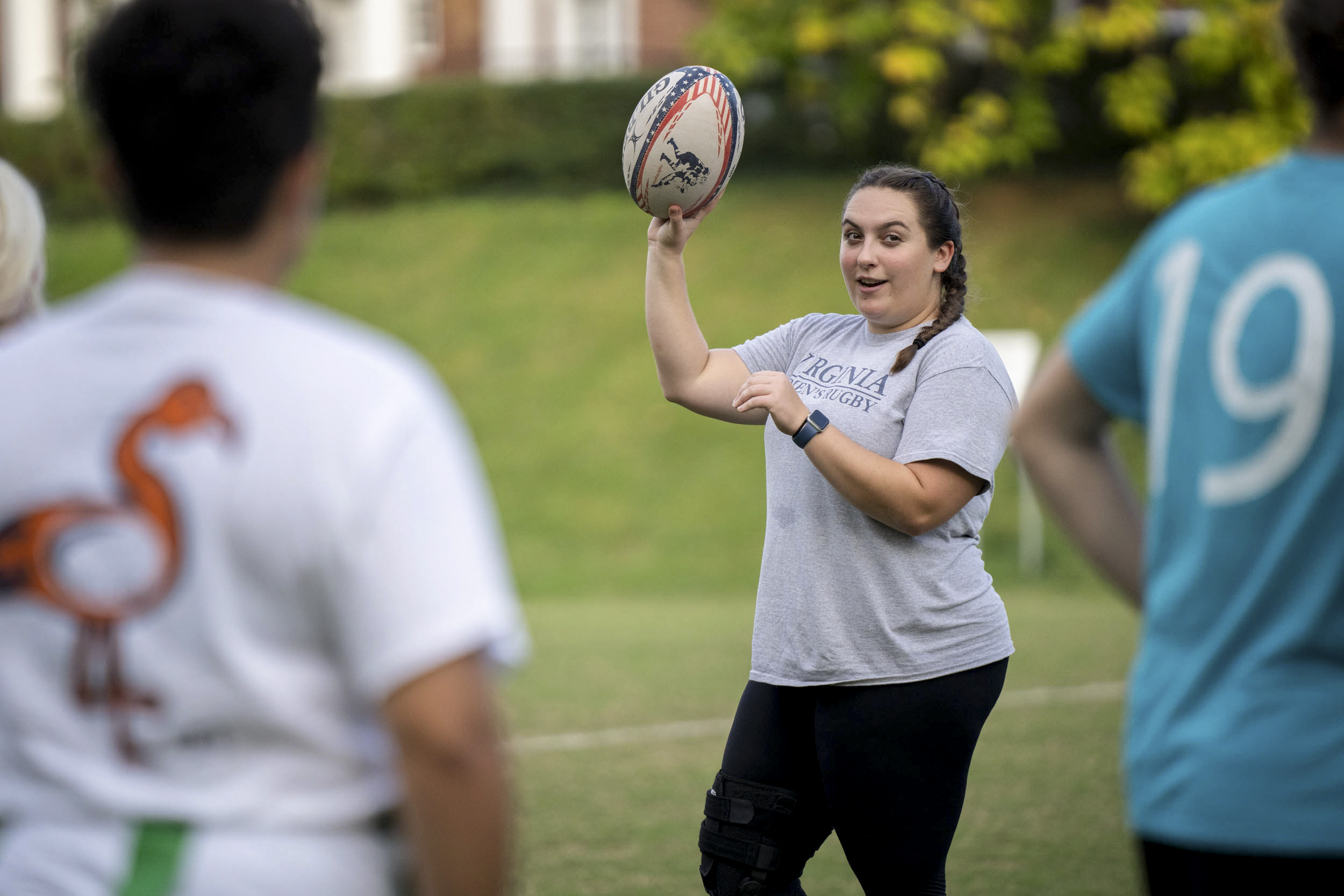 Alexis Ward talking to other Rugby players while holding a rugby ball in the air