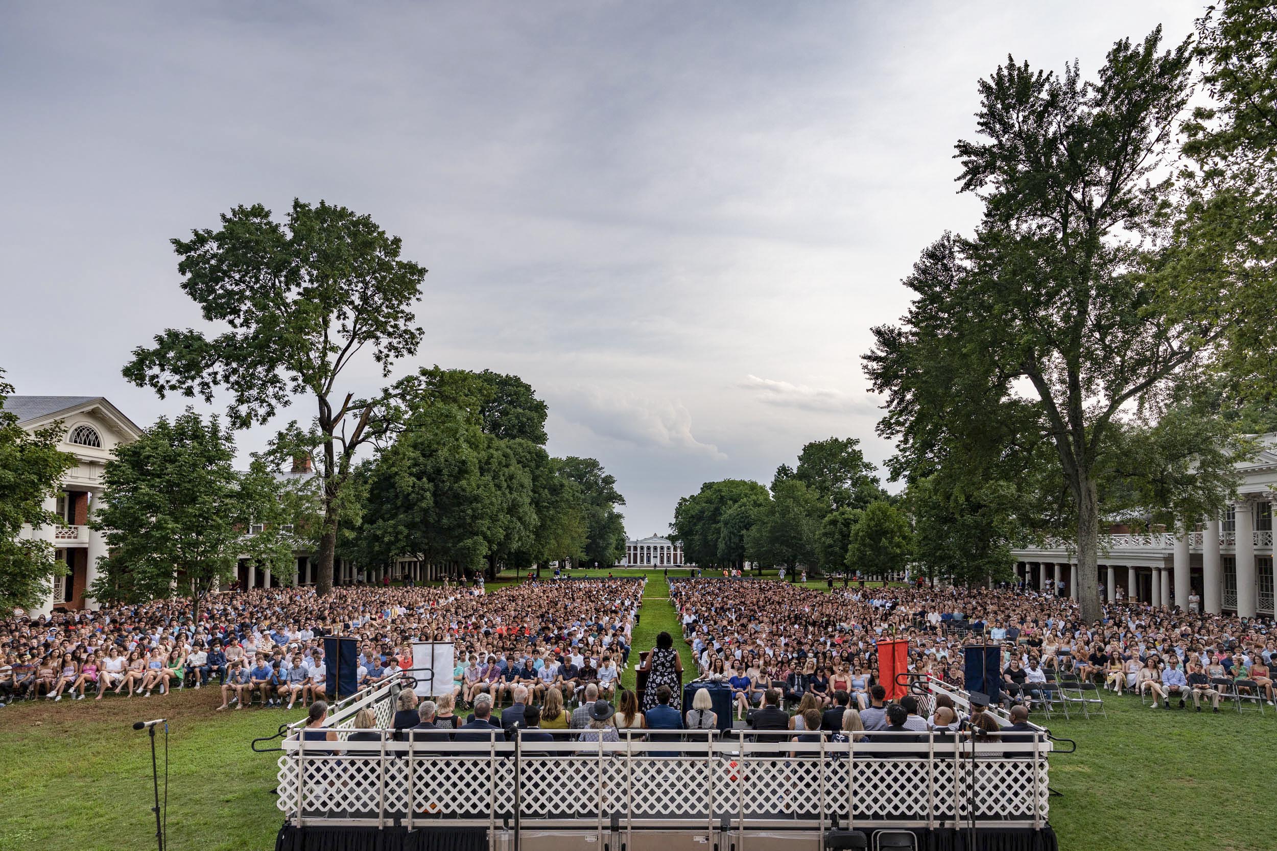 Students sitting in chairs on the lawn looking at a stage where a woman is giving a speech