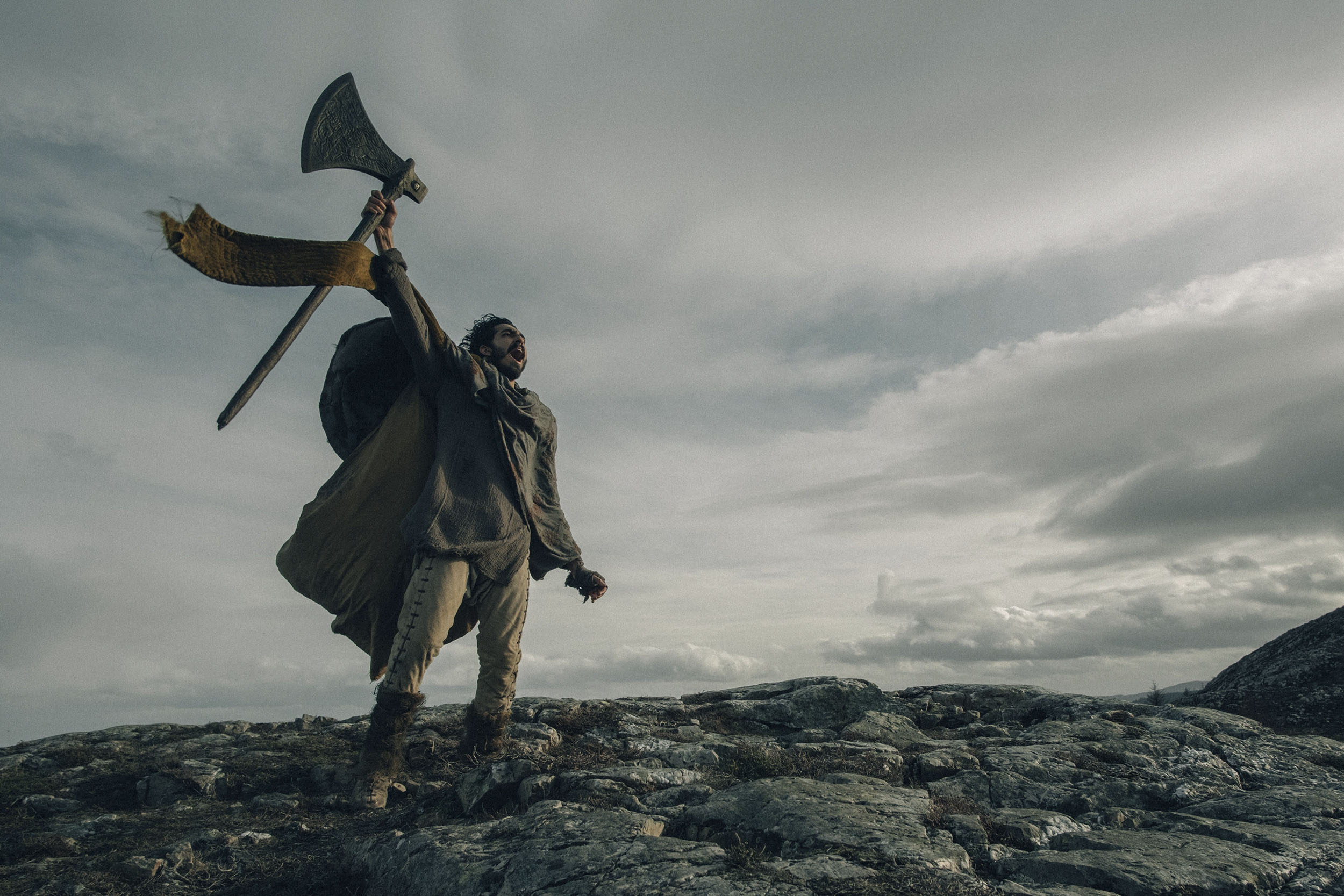 Dev Patel playing Gawain holds a huge axe in the air while he screams