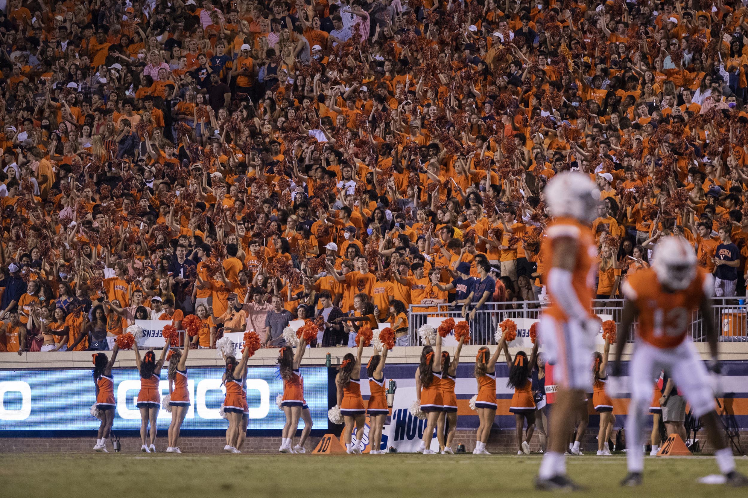 UVA crowd at football game in all orange while the cheerleaders cheer on the sidelines