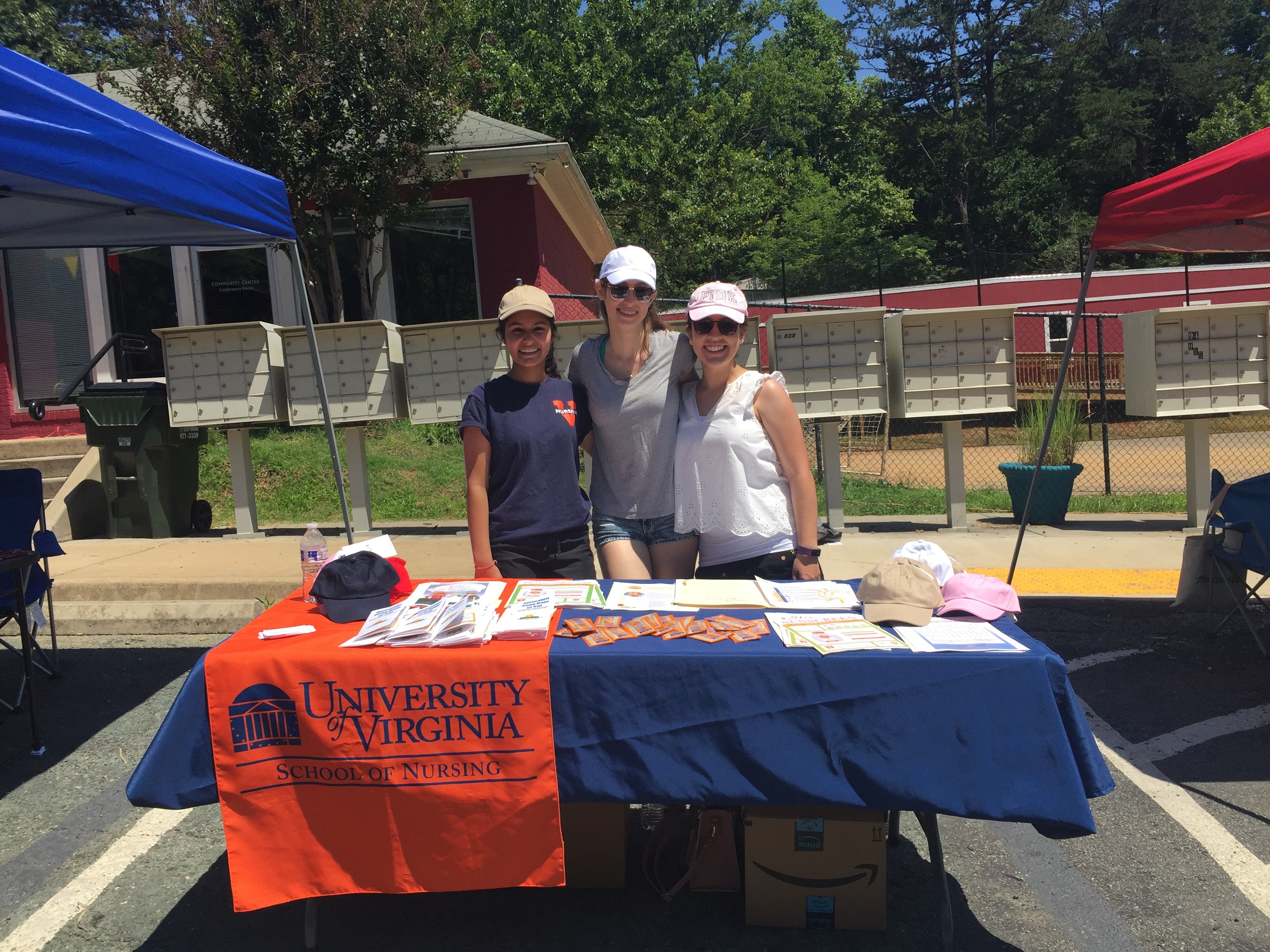 Sabrina Cumpian and Olivia Conn, with Esha Rawat, stand at a table handing out sun protection fliers and smaples