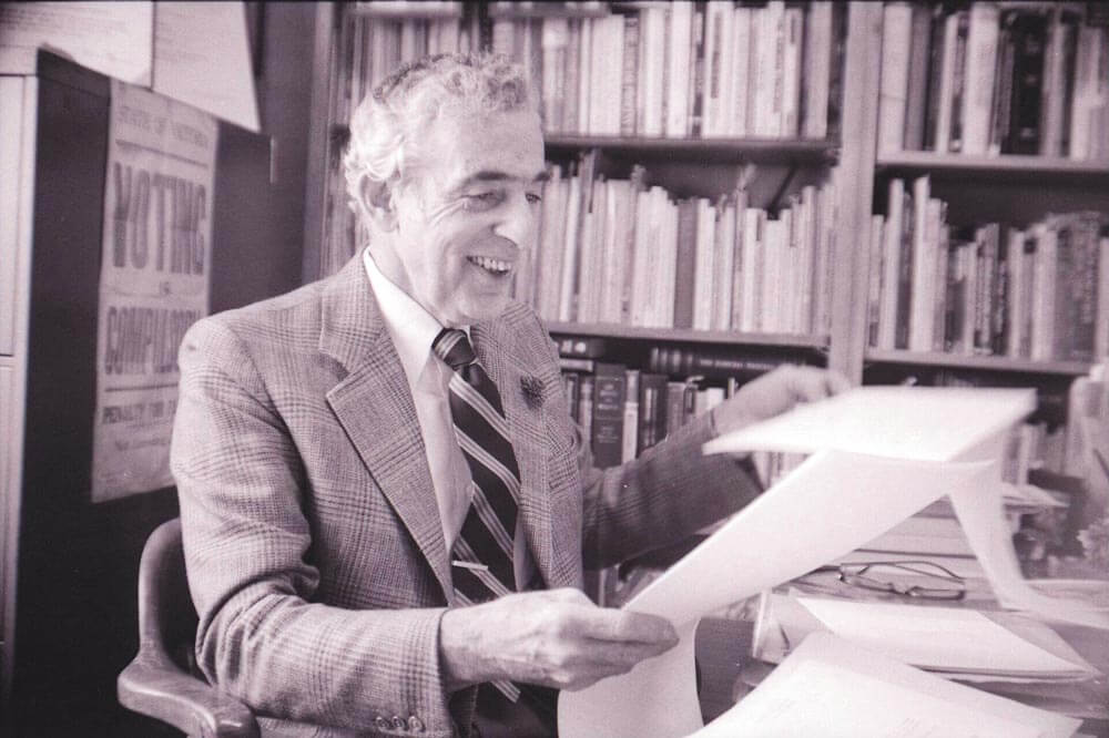 Black and white photo of Abraham sitting at a desk holding papers