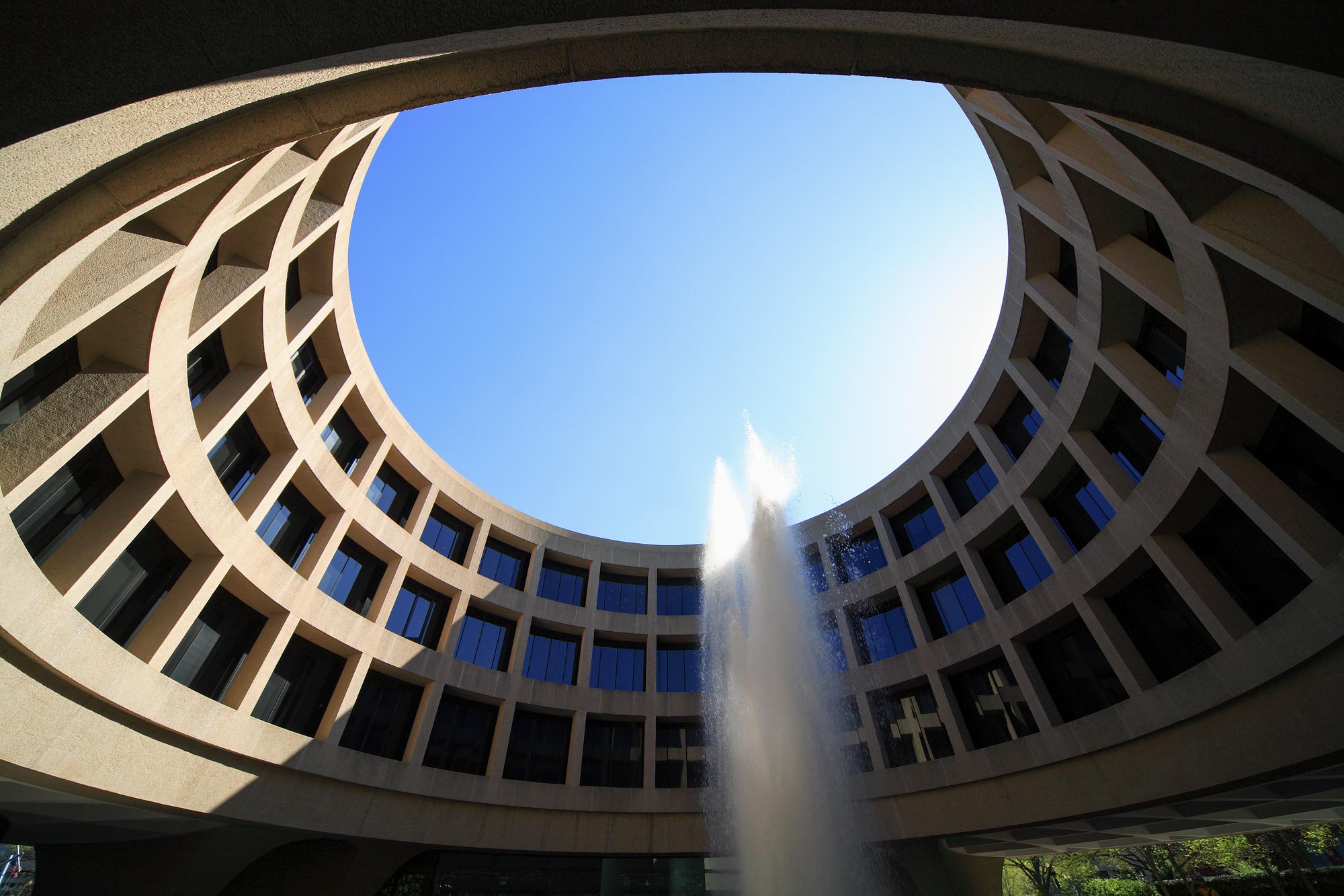 Looking up to the sky from inside of a circle building with a fountain in the middle and the sides of the building visible
