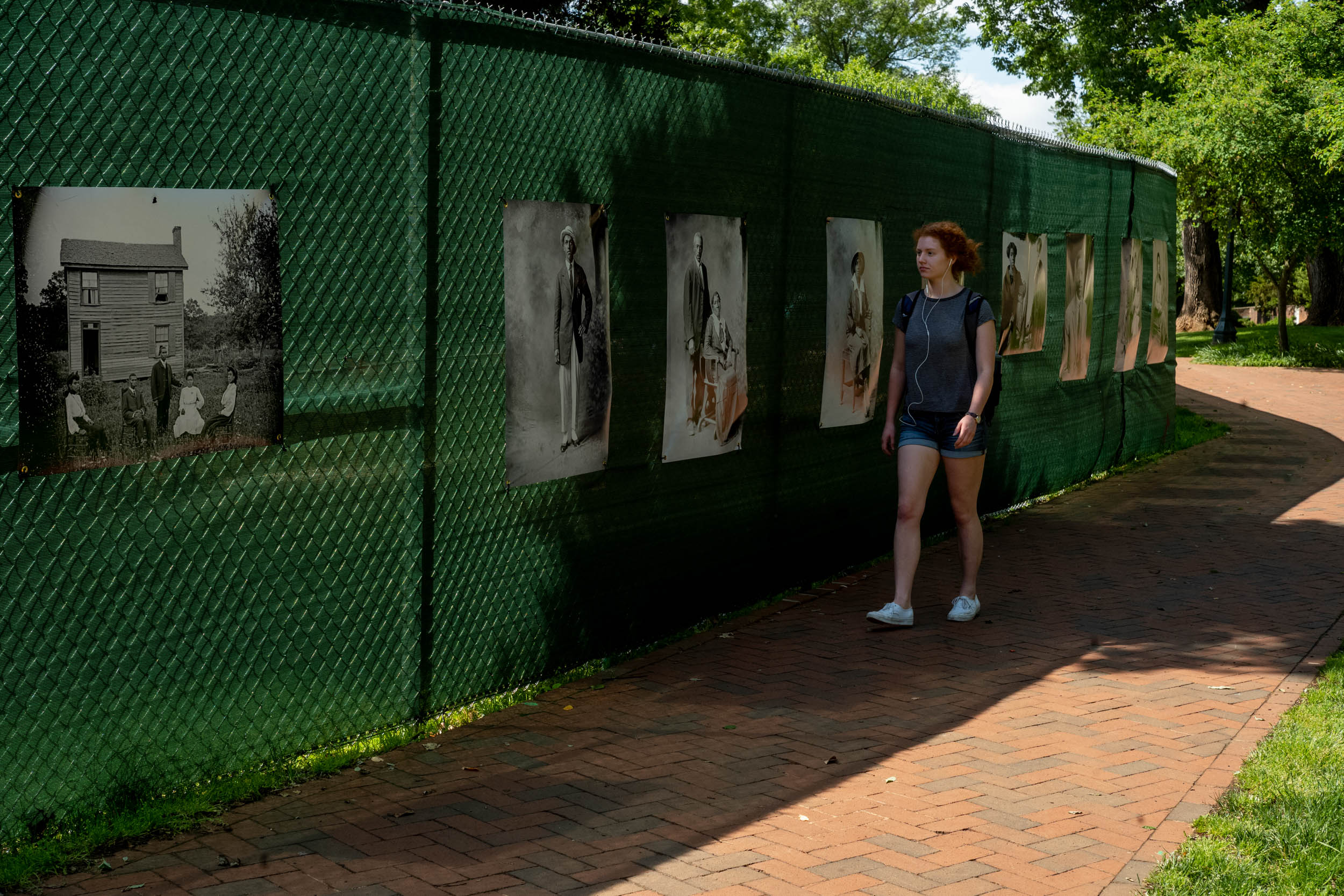 Black and white images hang from a chainlink fence as a student walks past
