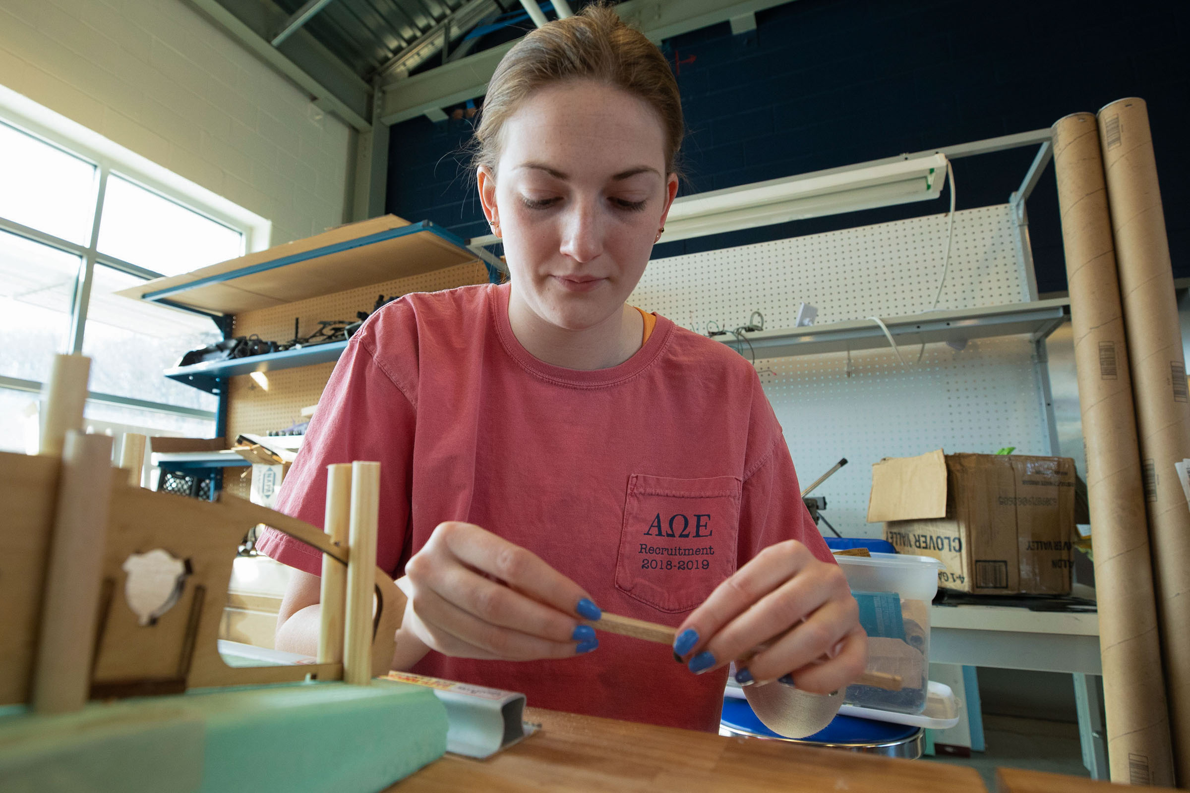 Haley Knowles is holding a small wooden component in a workshop