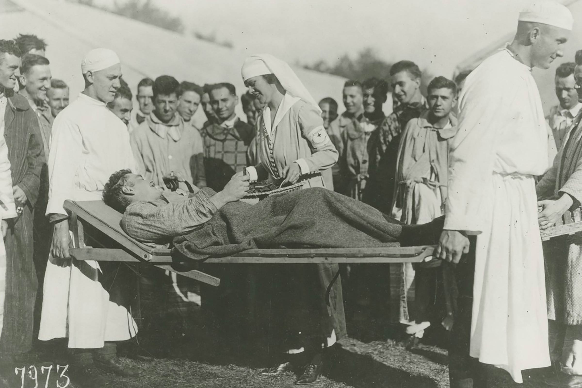 black and whit photo A nurse and fellow patients surround a patient nea