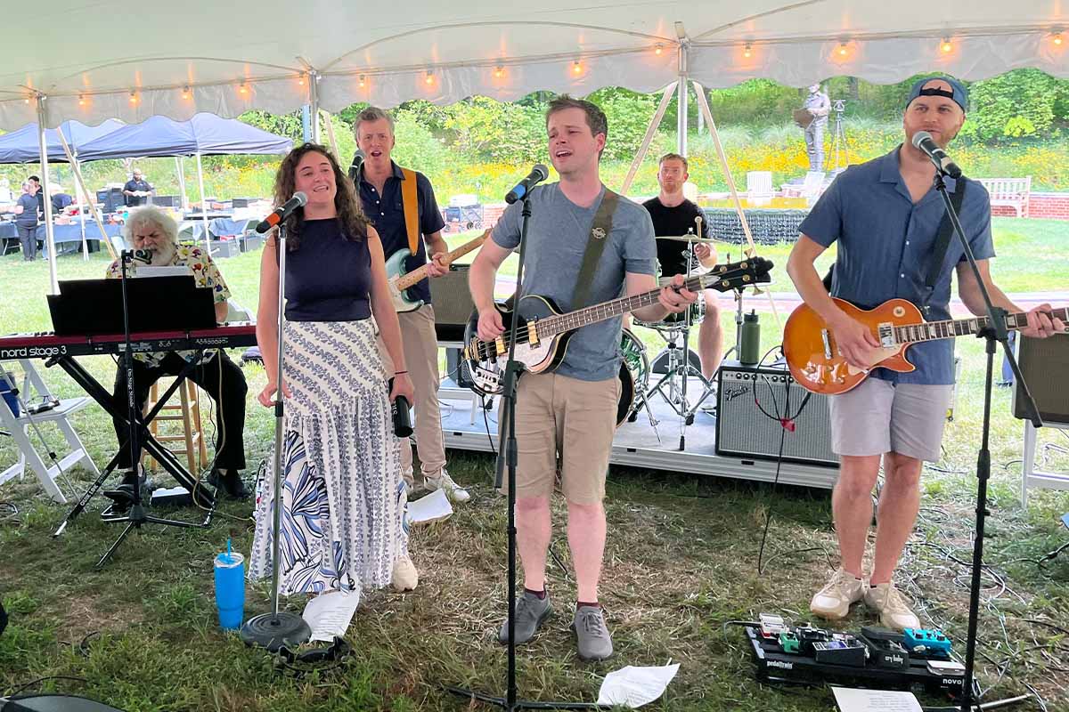 Ed Freeman, Skyler Clark-Hamel and bandmates perform songs outside under a canopy.