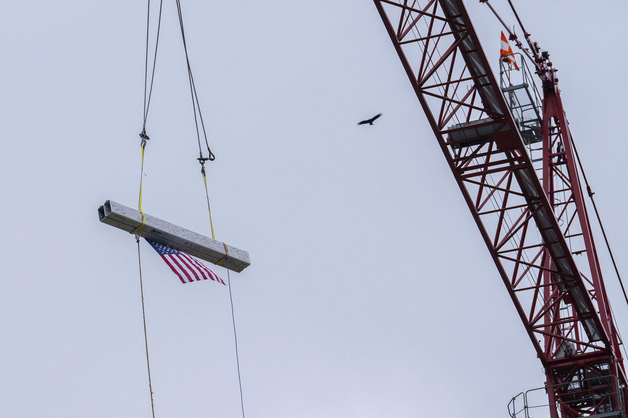 Flag and signed beam being raised by a crane.