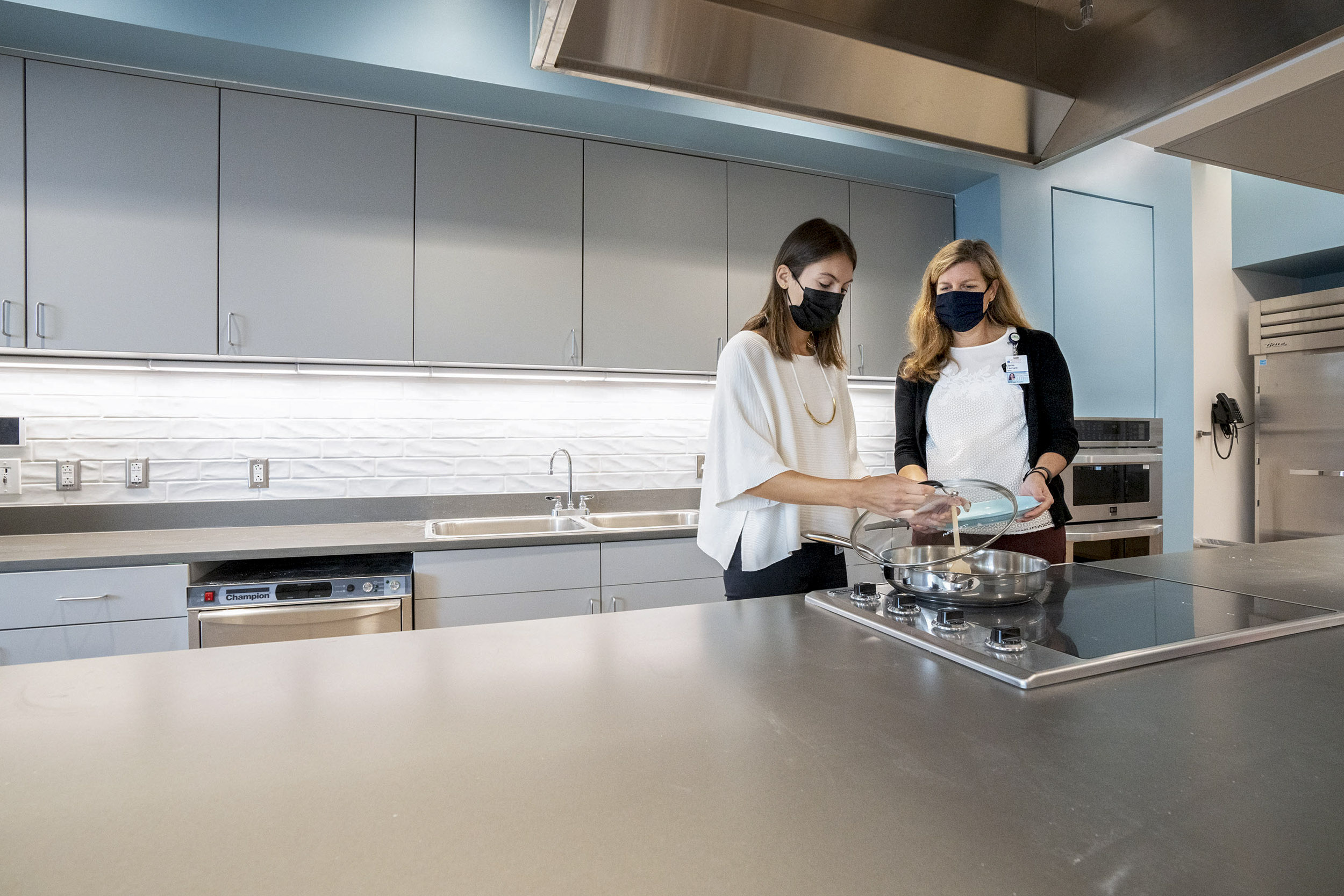 Two women in the Health and Wellness kitchen cooking a dish together on the stove