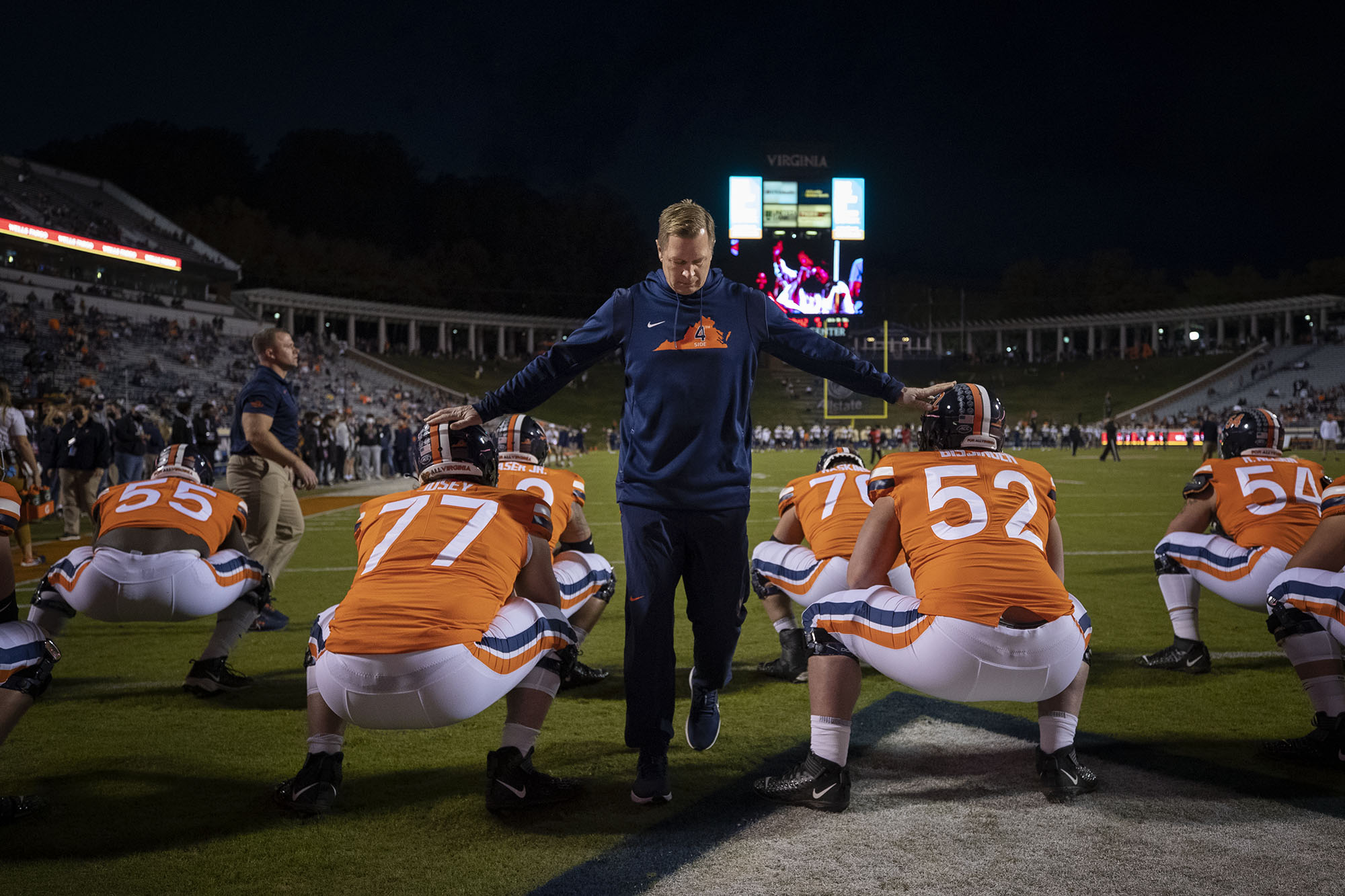 Bronco Mendenhall touching the helmets of two players while the whole team squats waiting for the game to start