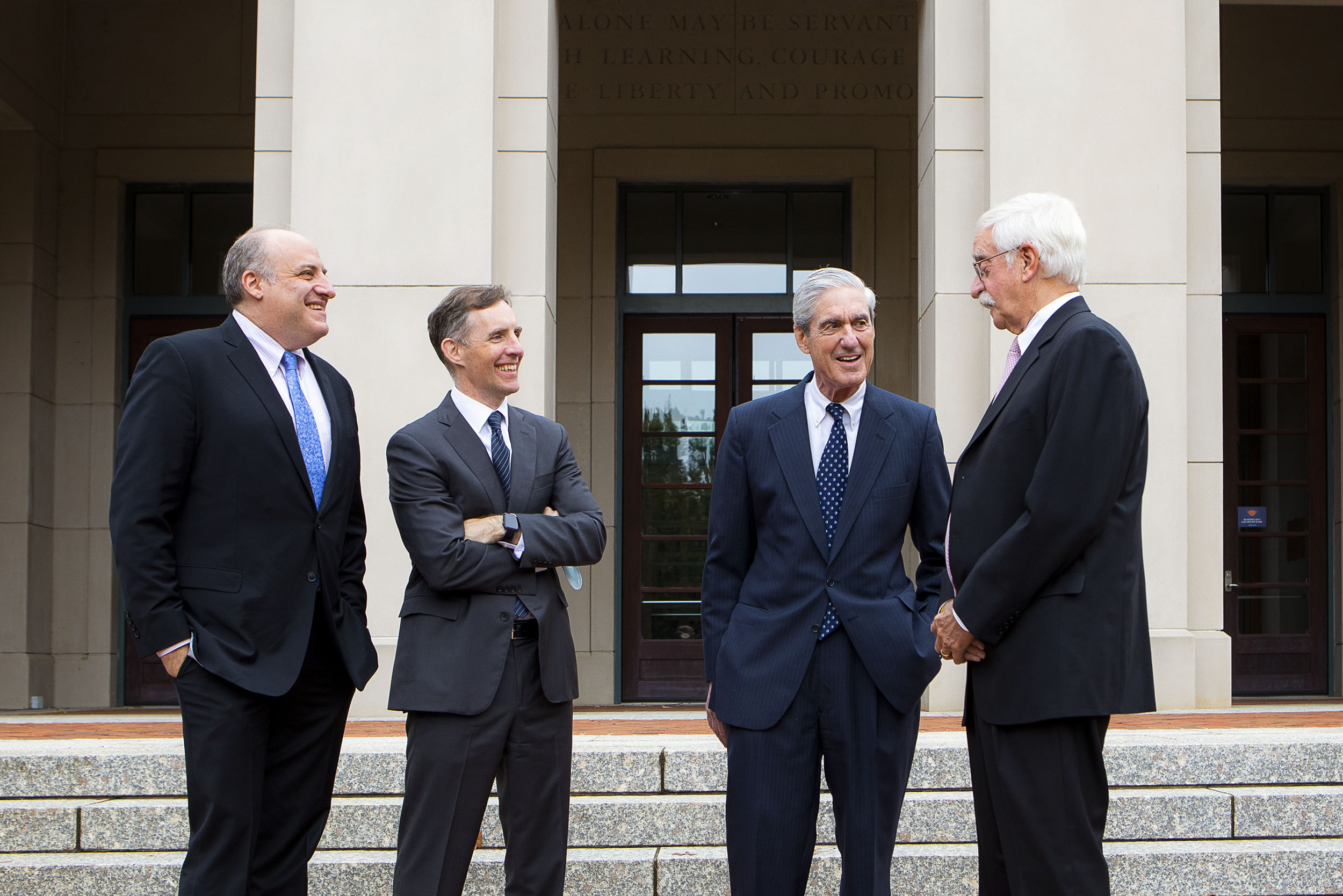 Andrew Goldstein, Aaron Zebley, Robert Mueller and Jim Quarles talking outside of a building in a half circle