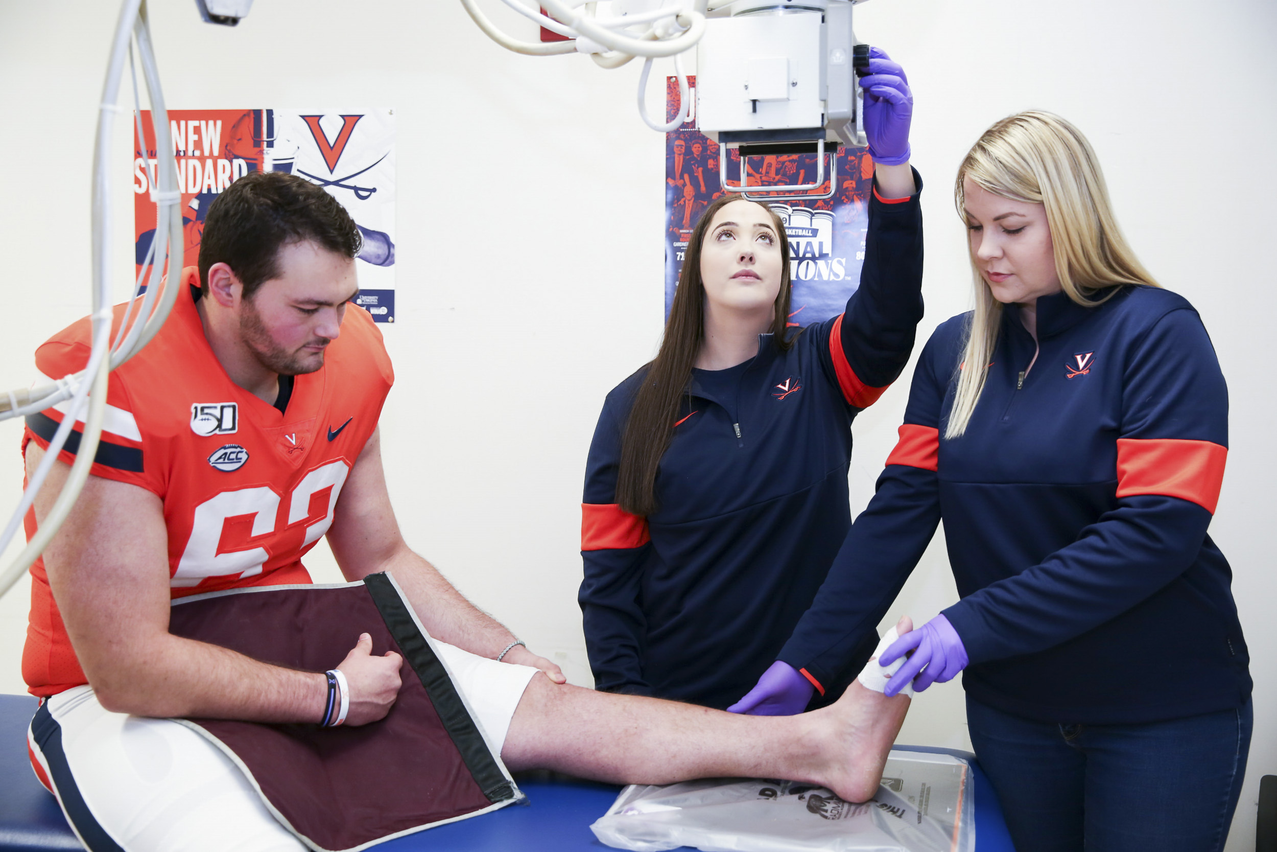 Two Athletic trainers taking an x-ray of a UVA football players ankle