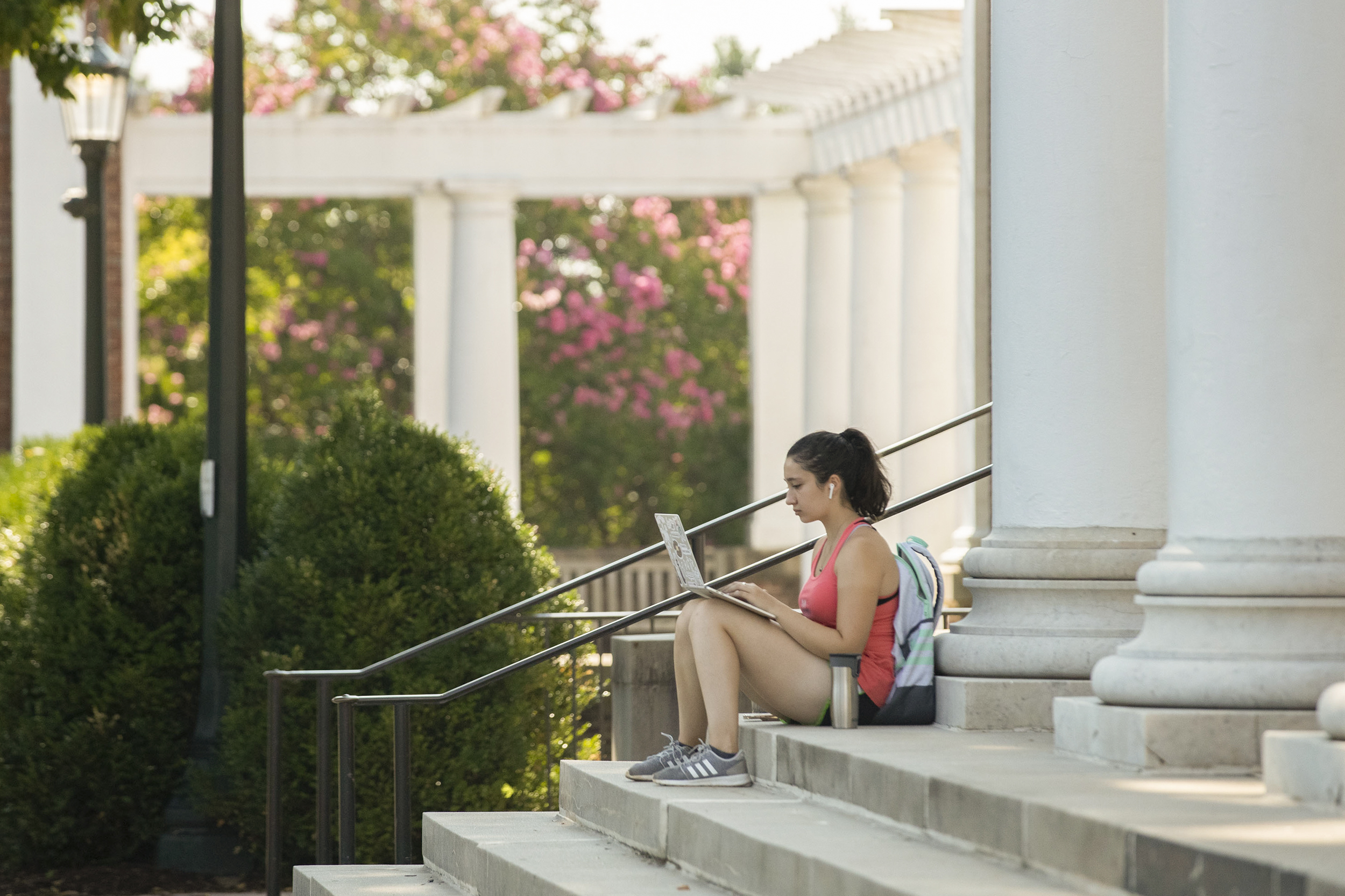 Student sitting on the steps at the base of a column working on their laptop
