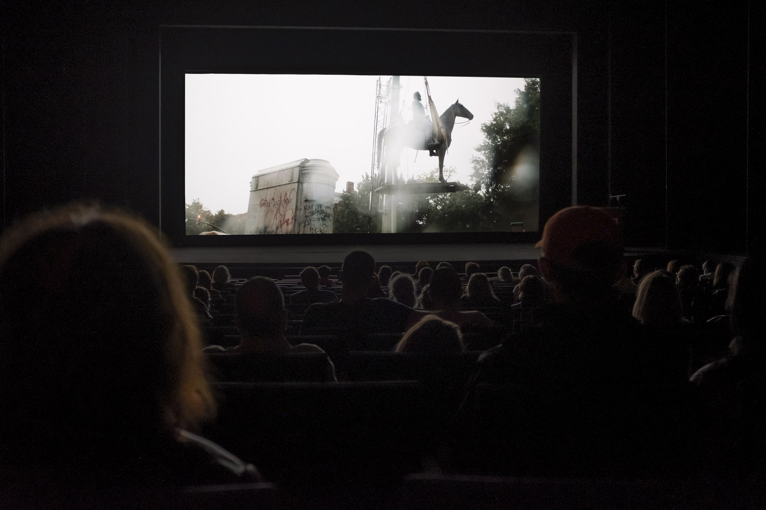 People in a theatre watching Civil War monuments being removed on a movie screen