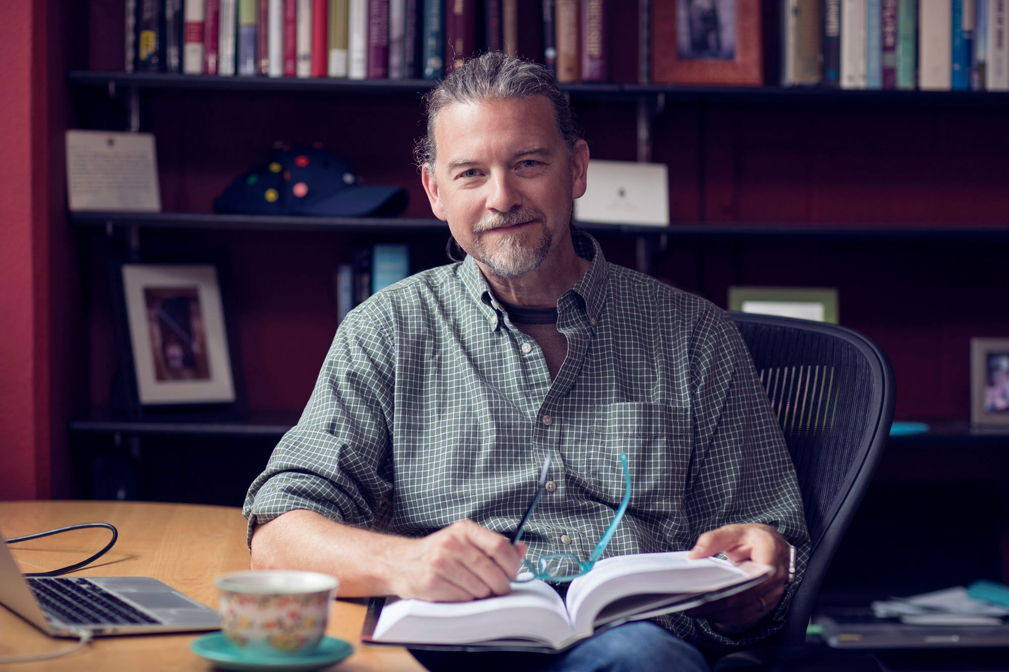 James Coan sits in a chair looking at the camera holding a book