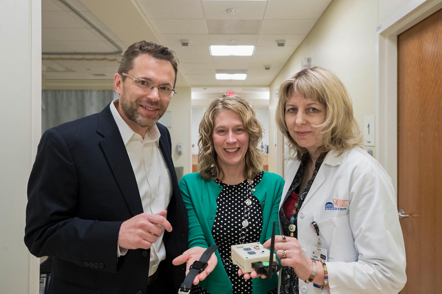 John Lach, Virginia LeBaron, and Leslie Blackhall stand in a hallway smiling for the camera while holding a pain management device