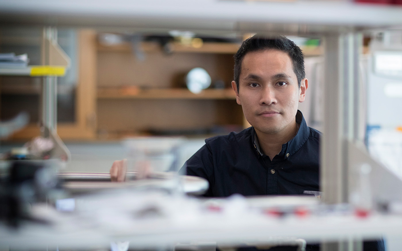 Ken Hsu looking at camera through metal lab shelves