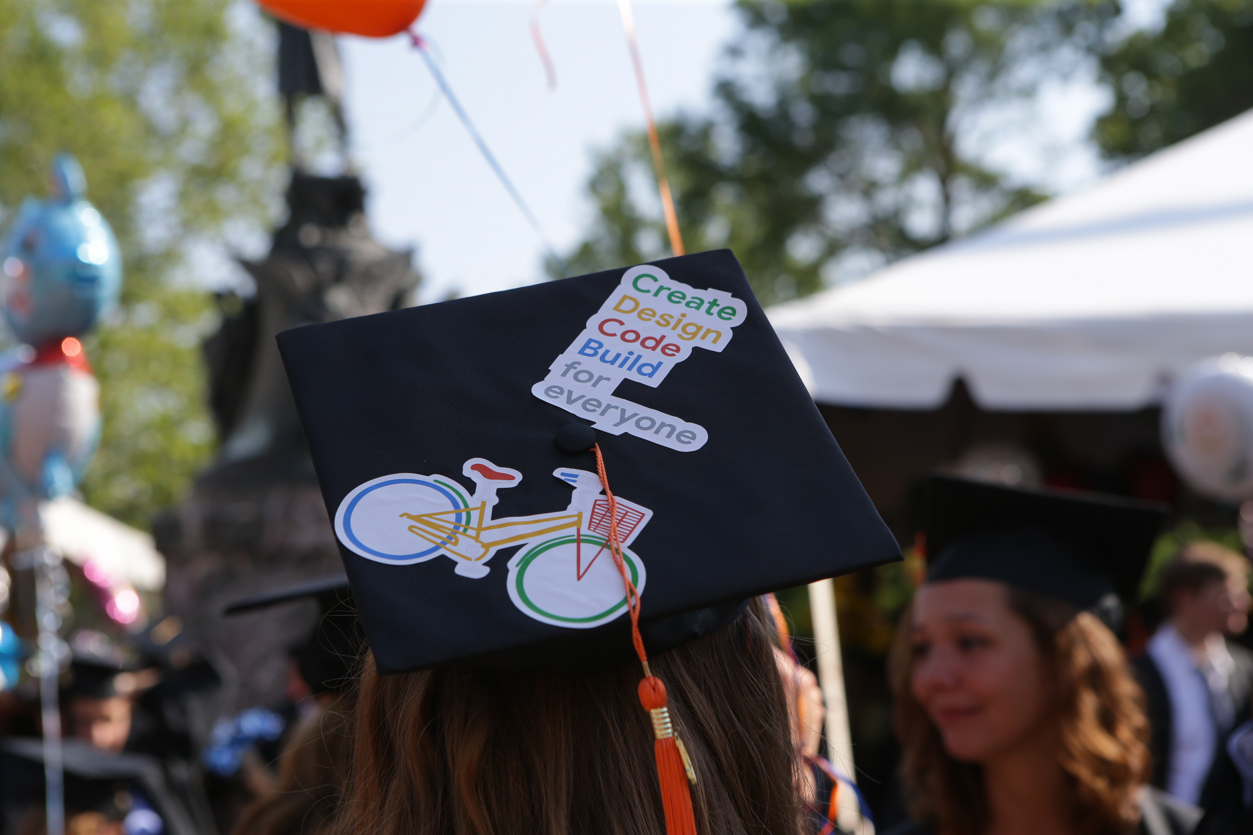 Graduation cap that reads Create Design code build for everyone with a multicolored bicycle