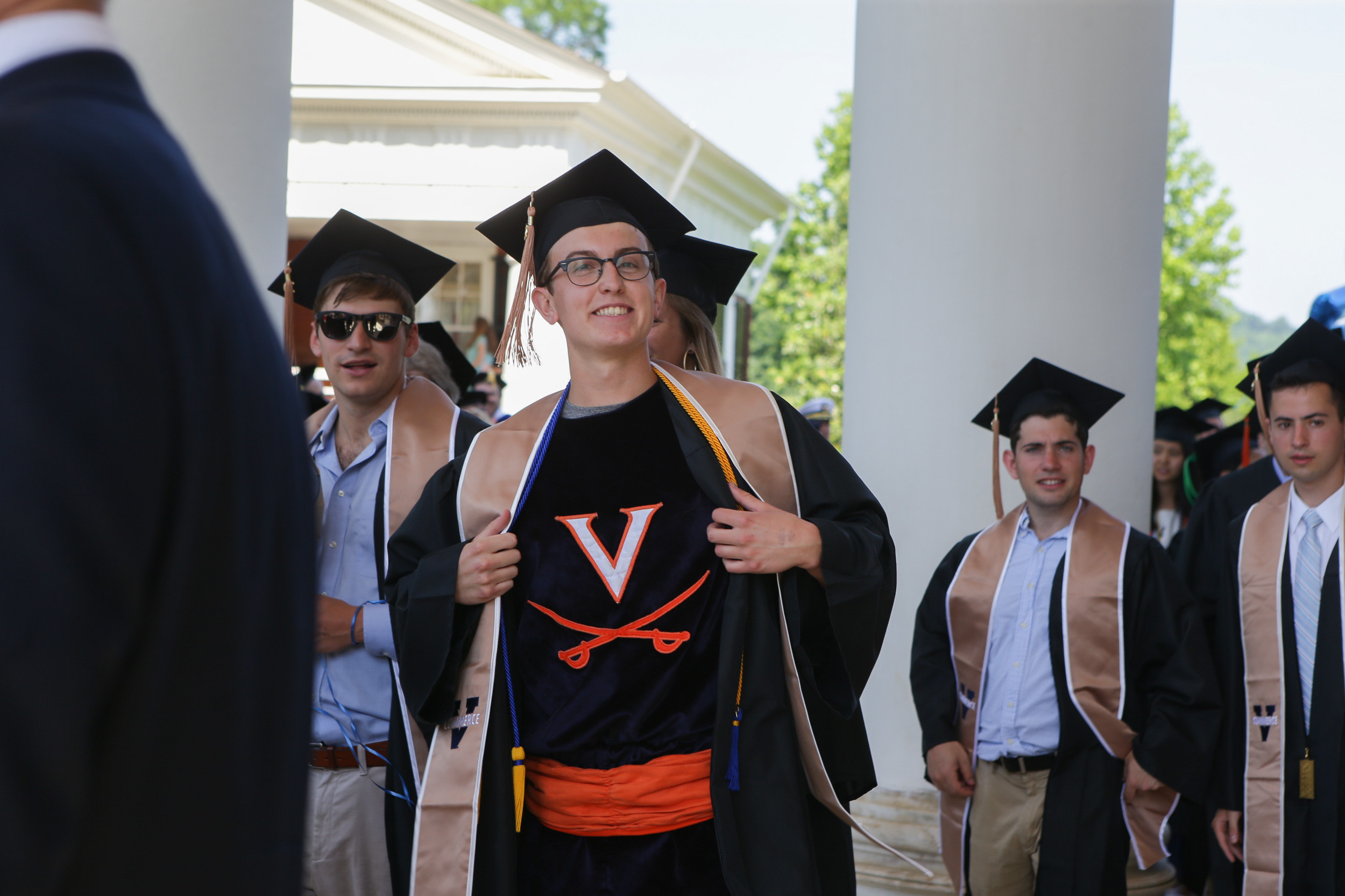 Man opens his graduation robe to see a V saber shirt and orange cumberbun