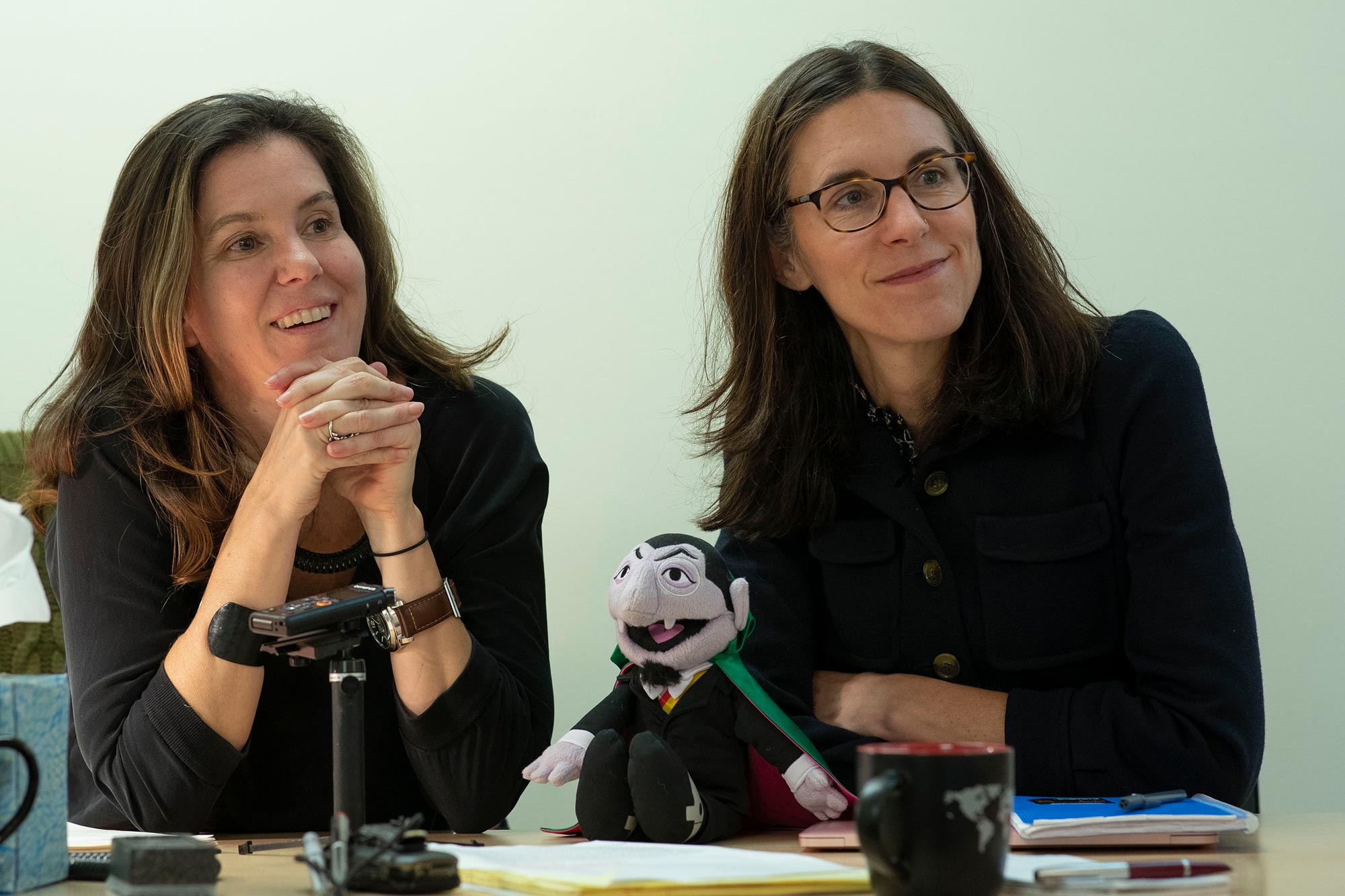 Kirsten Gelsdorf and Lucy Bassett sitting at a table together listening to someone speak 