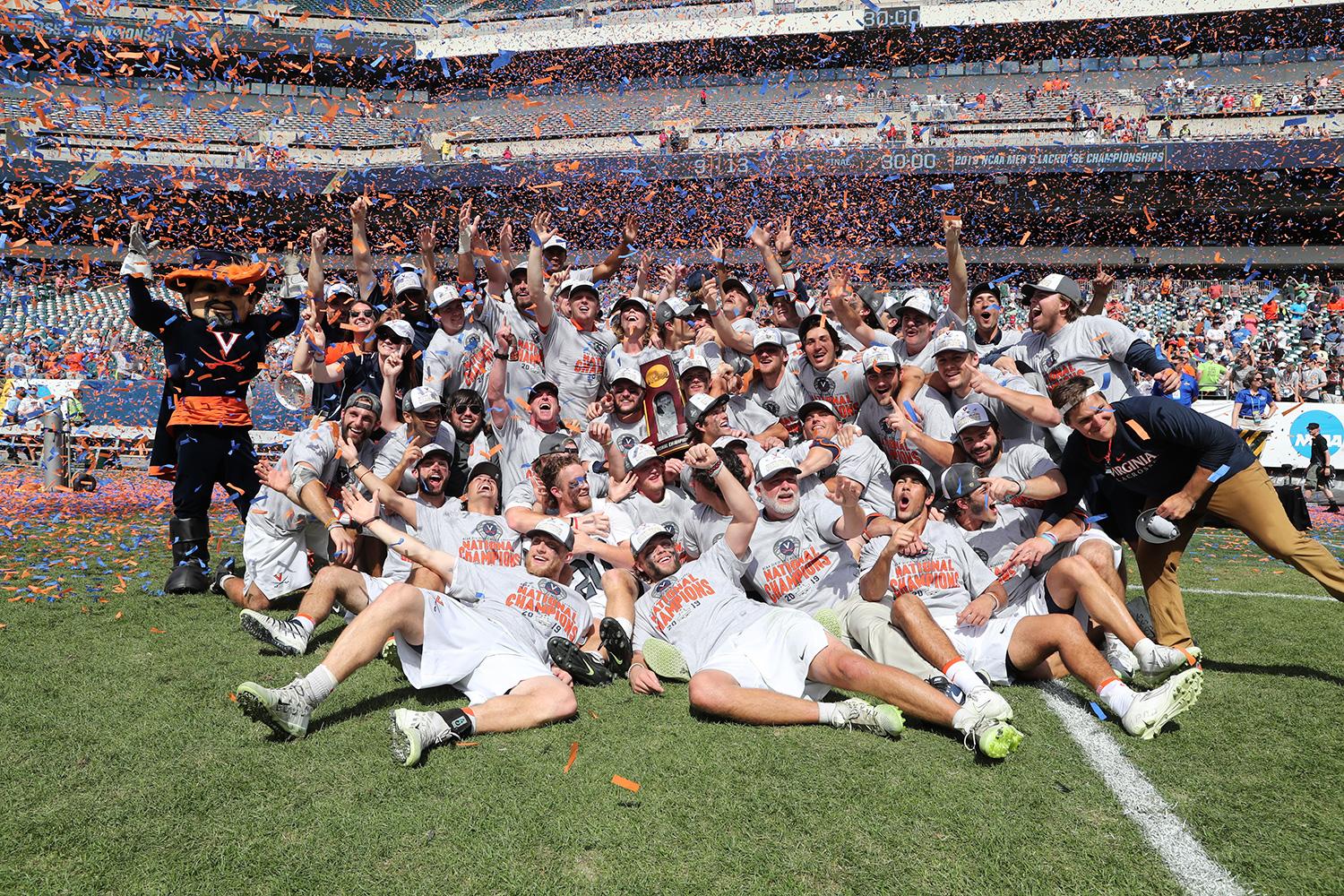 The UVA men’s lacrosse team celebrate on the field with a team photo while holding the NCAA trophy