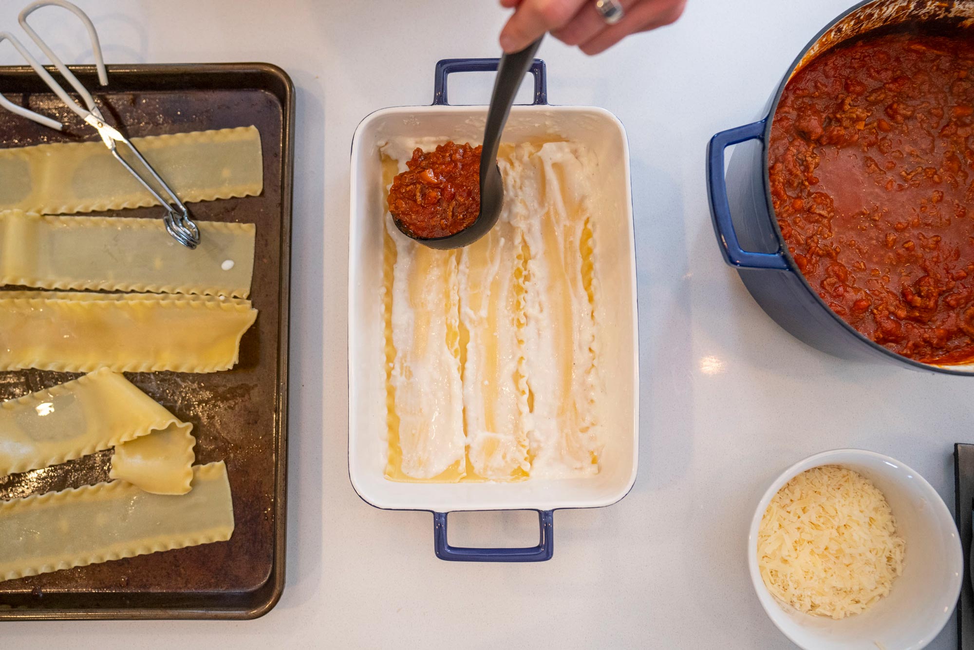 Person spreading sauce on top of lasagna noodles in a pan
