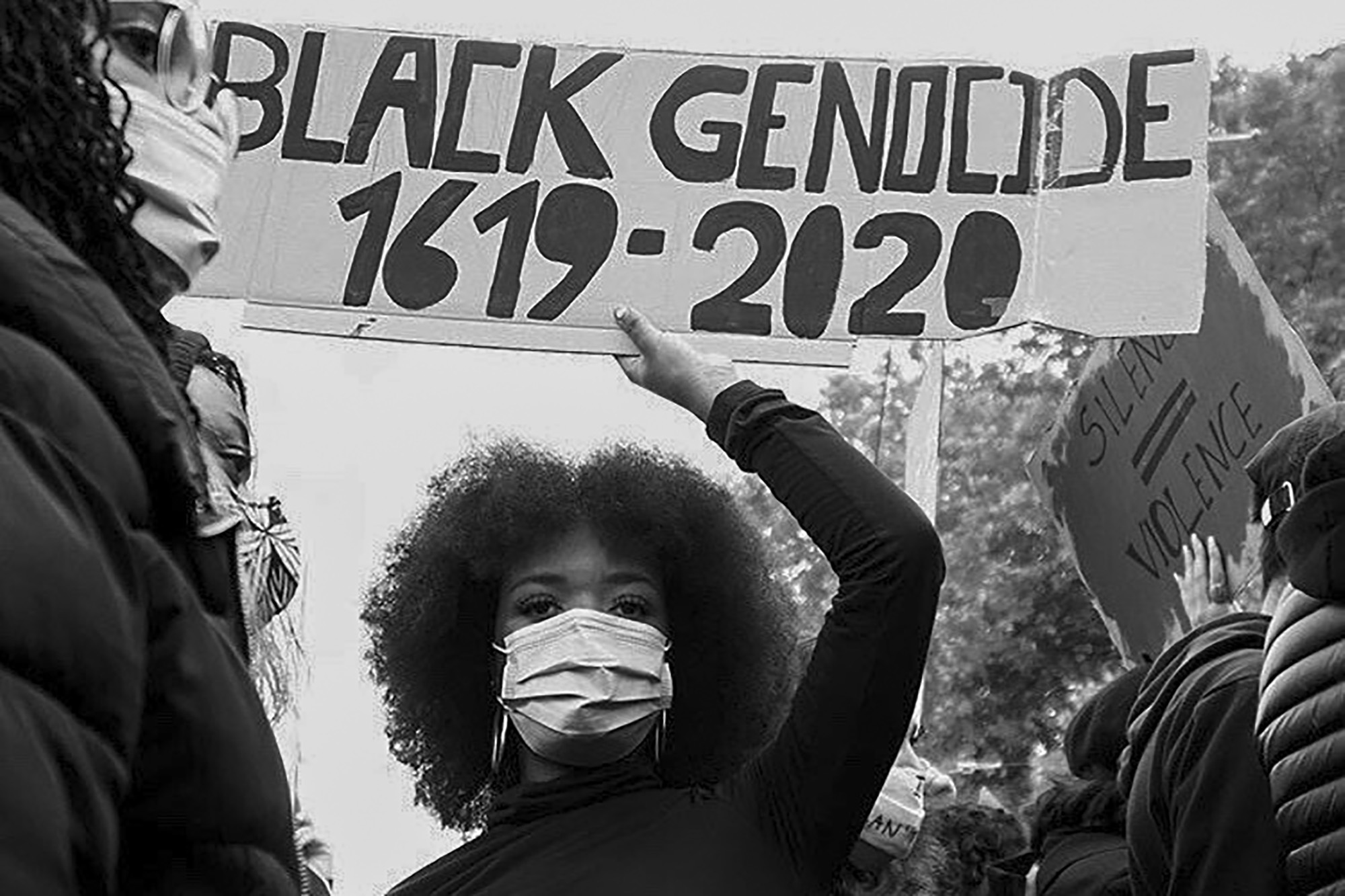 African American woman carrying a sign above their head that says Black Genocide 1619-2020
