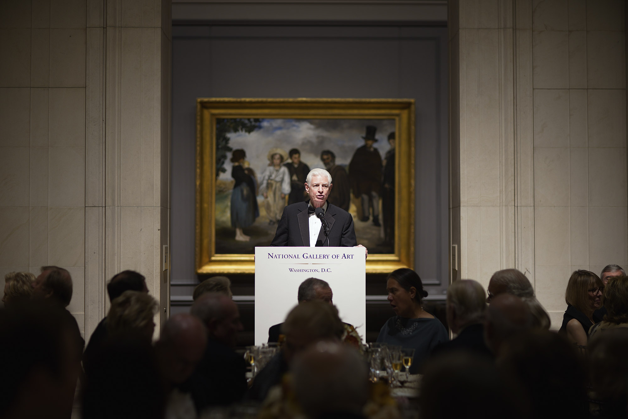 Beinecke stands at a podium giving a speech at the National Gallery of Art