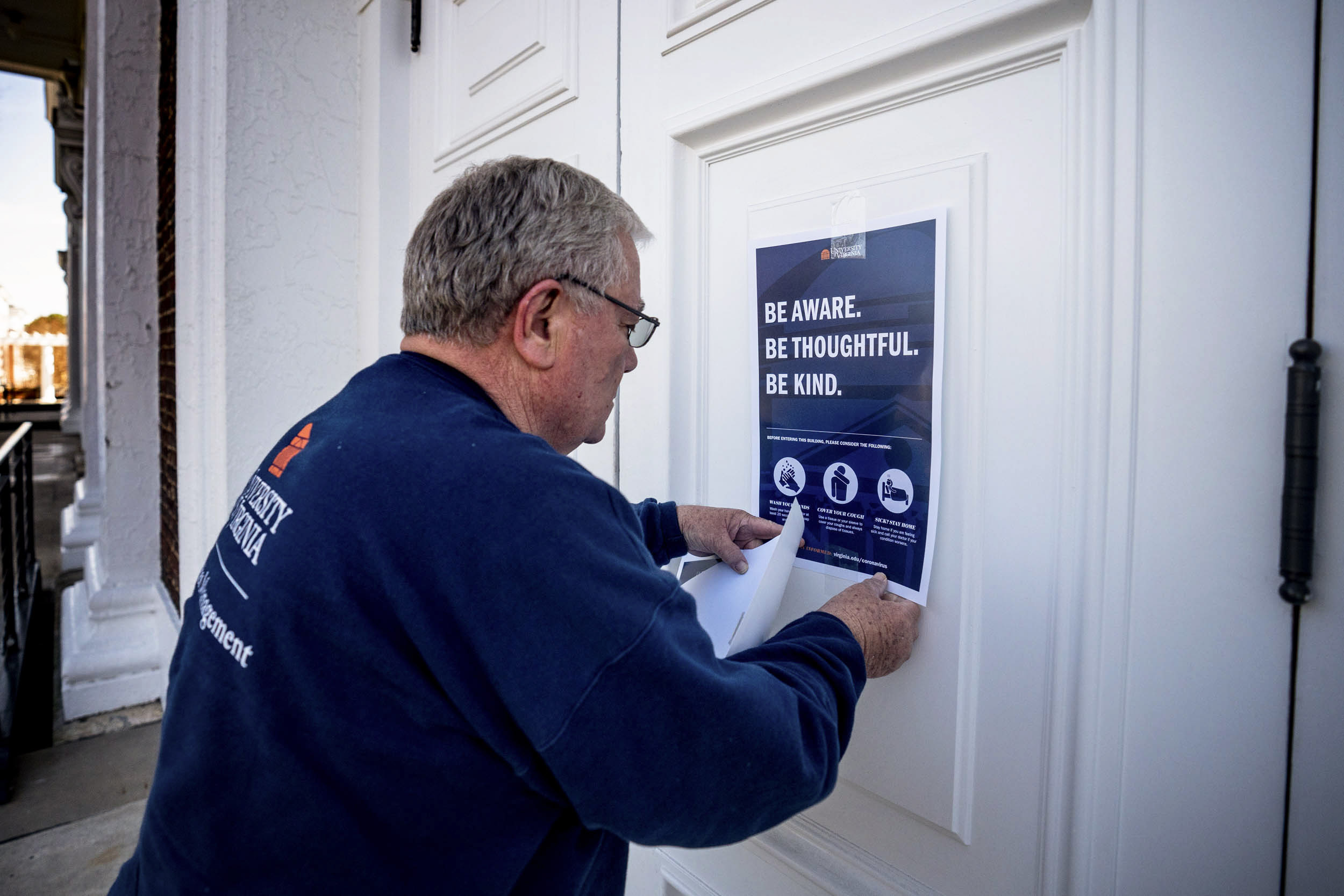 UVA staff member placing a sign on the door of a UVA building