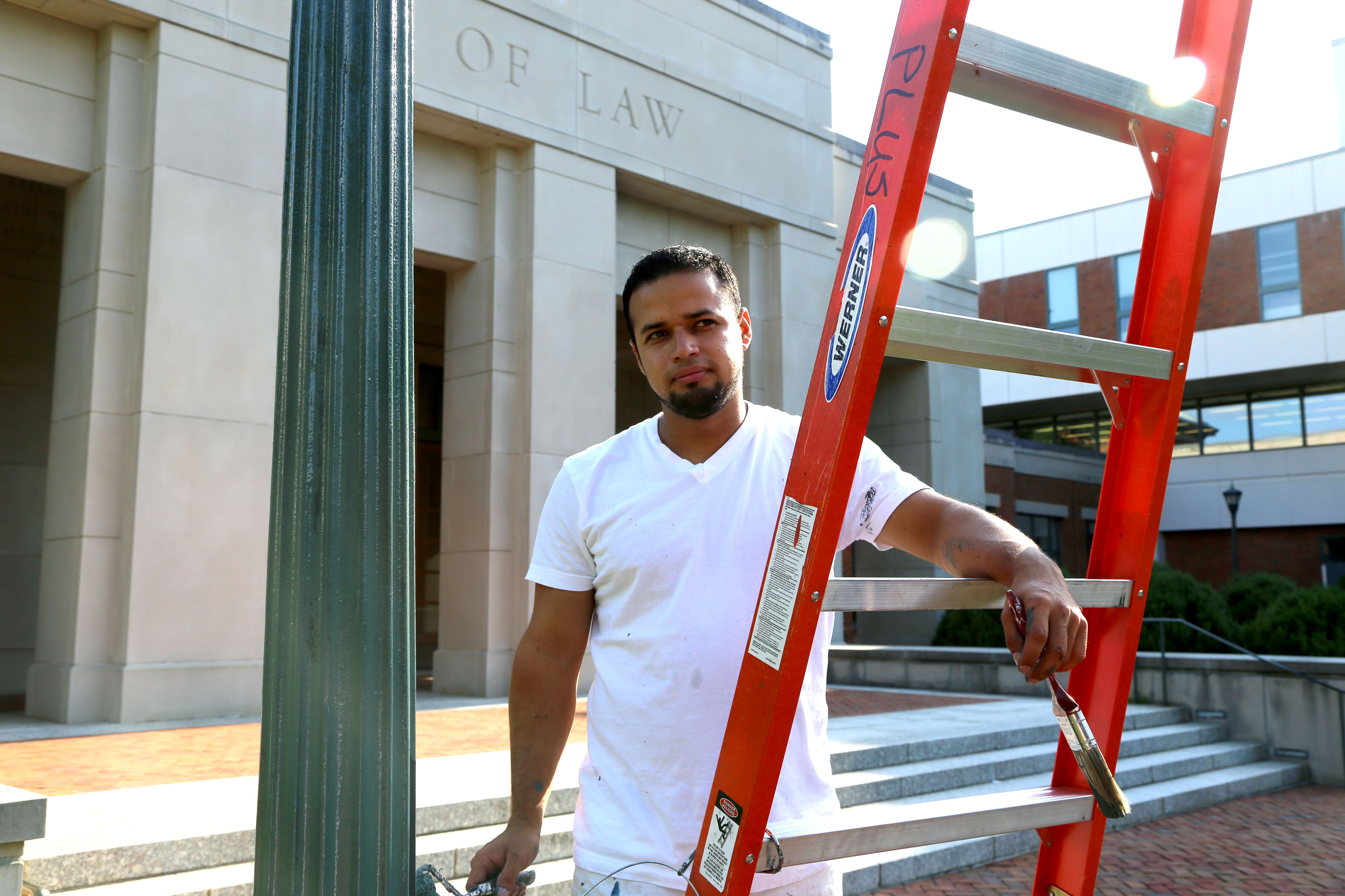 Man holding a ladder near a light pole in front of the school of lawn building looking at the camera