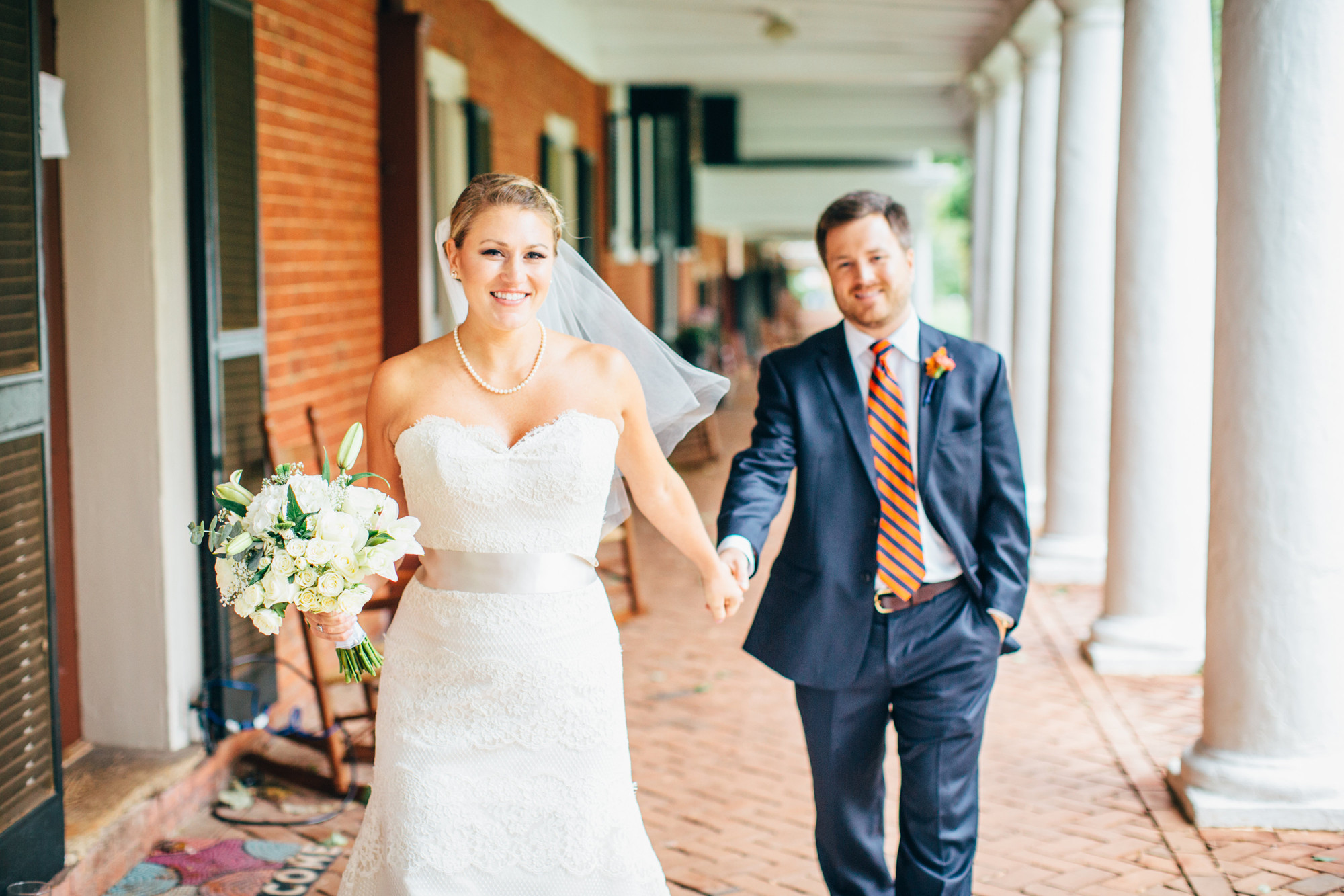 Bride and Groom walk the lawn sidewalks  holding hands