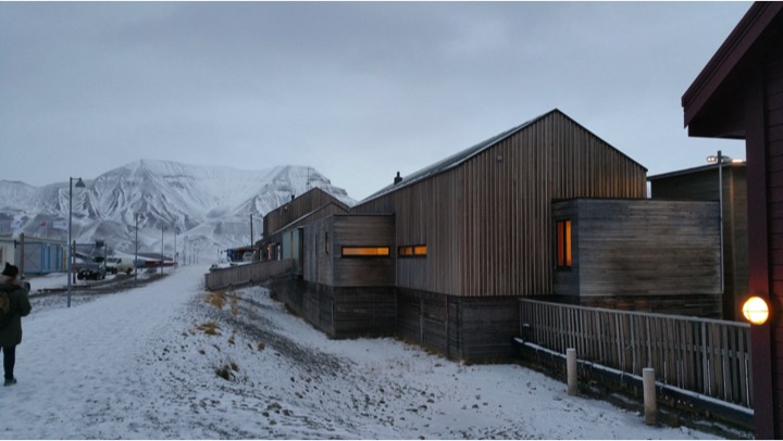 wooden buildings in Longyearbyen village while the ground and mountain are covered in snow