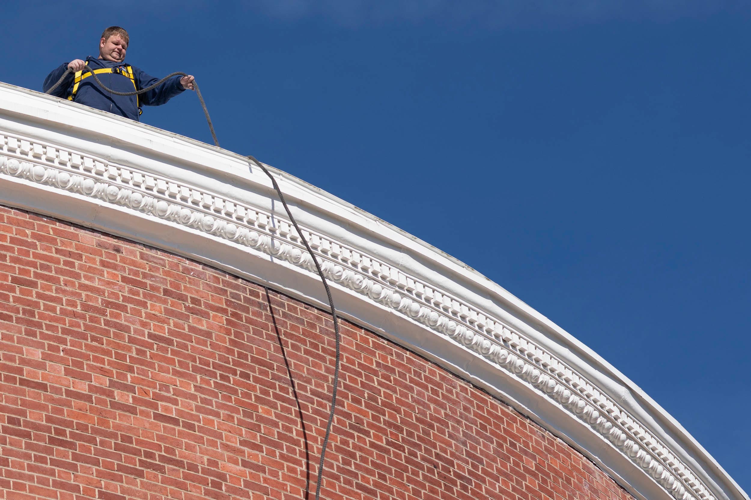 Man in a harness on top of the Rotunda helps a cord go over the side of the building