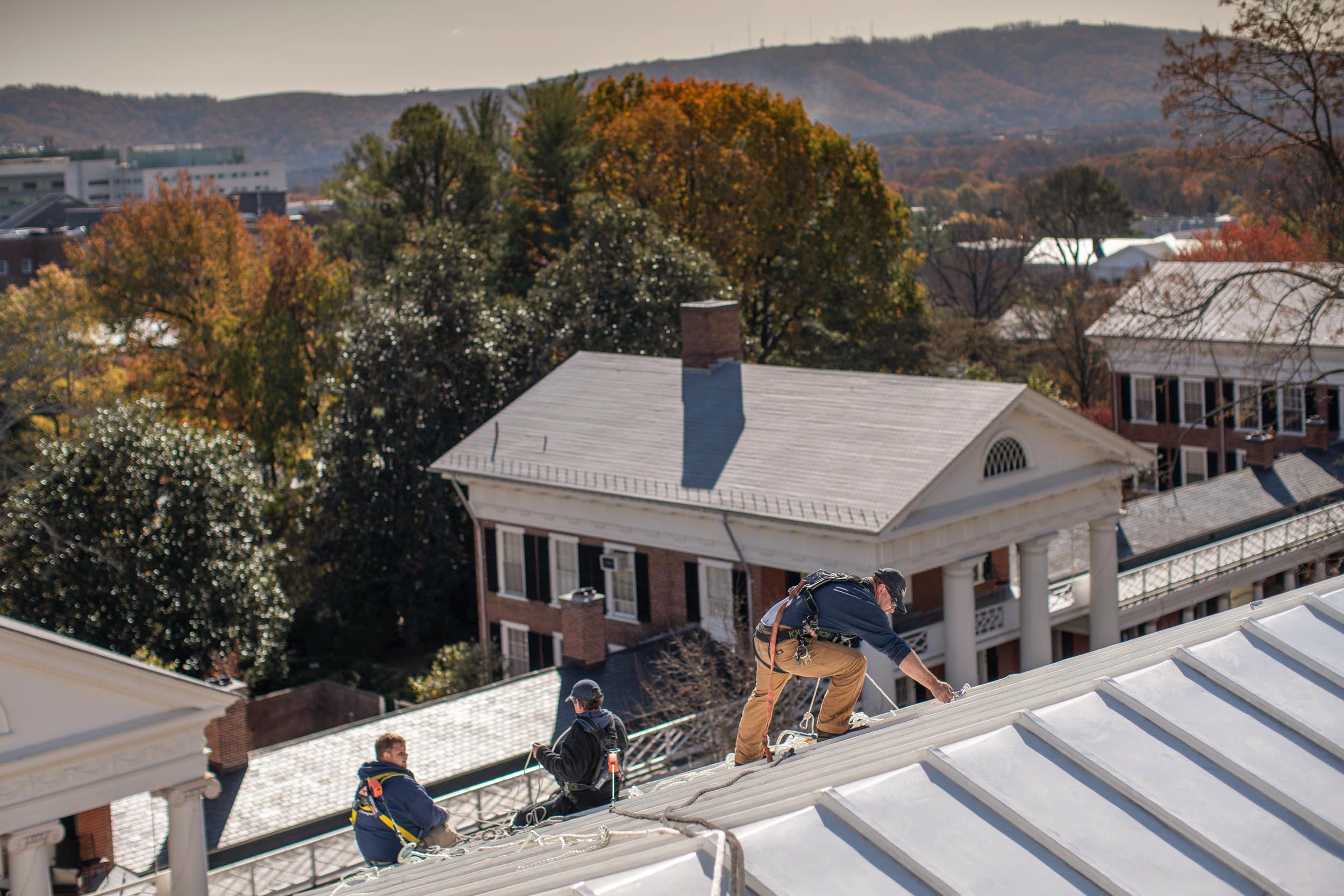 People in harnesses walking on the roof of a lawn building doing maintenance 