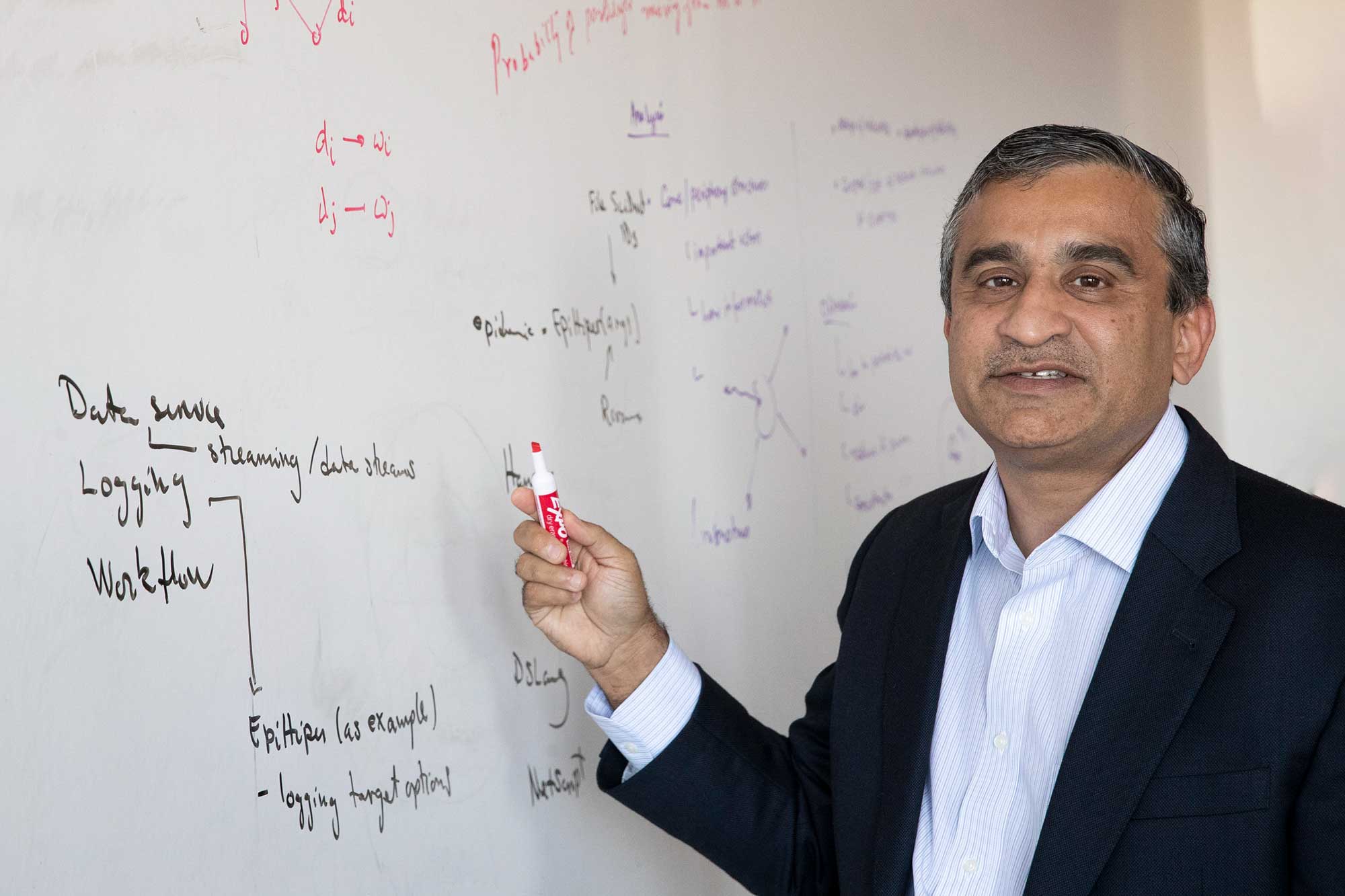 Madhav Marathe standing next to a white board holding a dry erase marker while looking at the camera