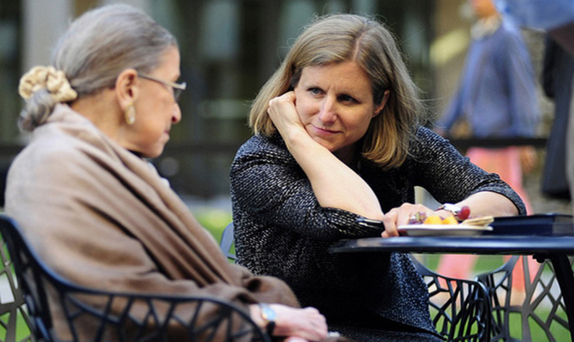 Elizabeth Magill sits at a table talking to Ruth Bader Ginsburg
