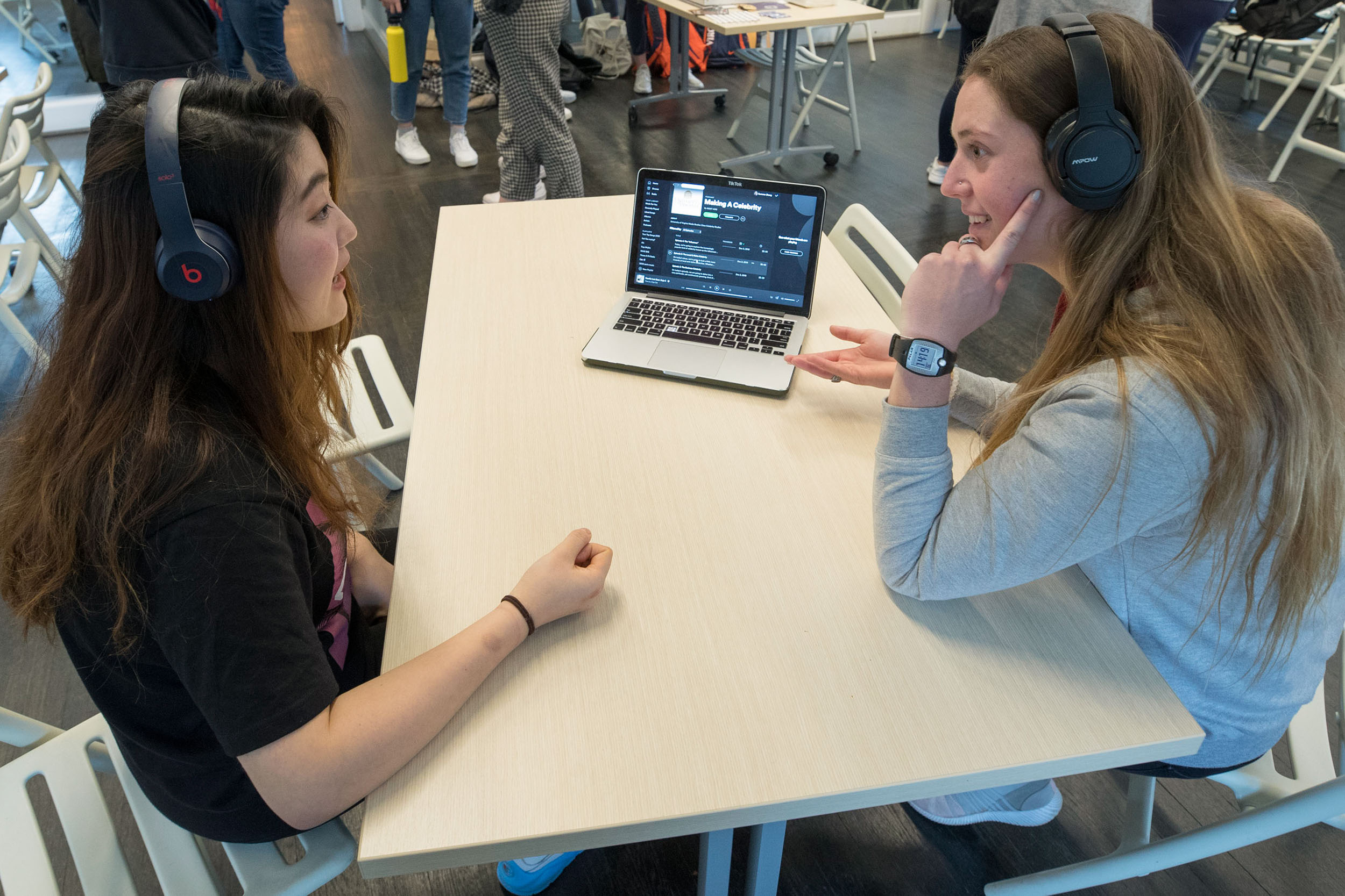 two uva students sit at the same table wearing headphones and working on one laptop