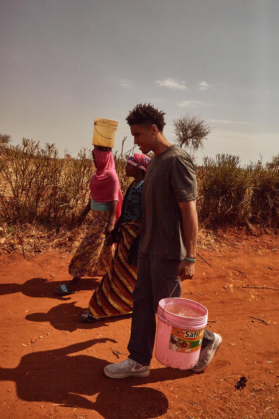Malcolm Brogdon carrying water in five gallon buckets along side two women in Africa