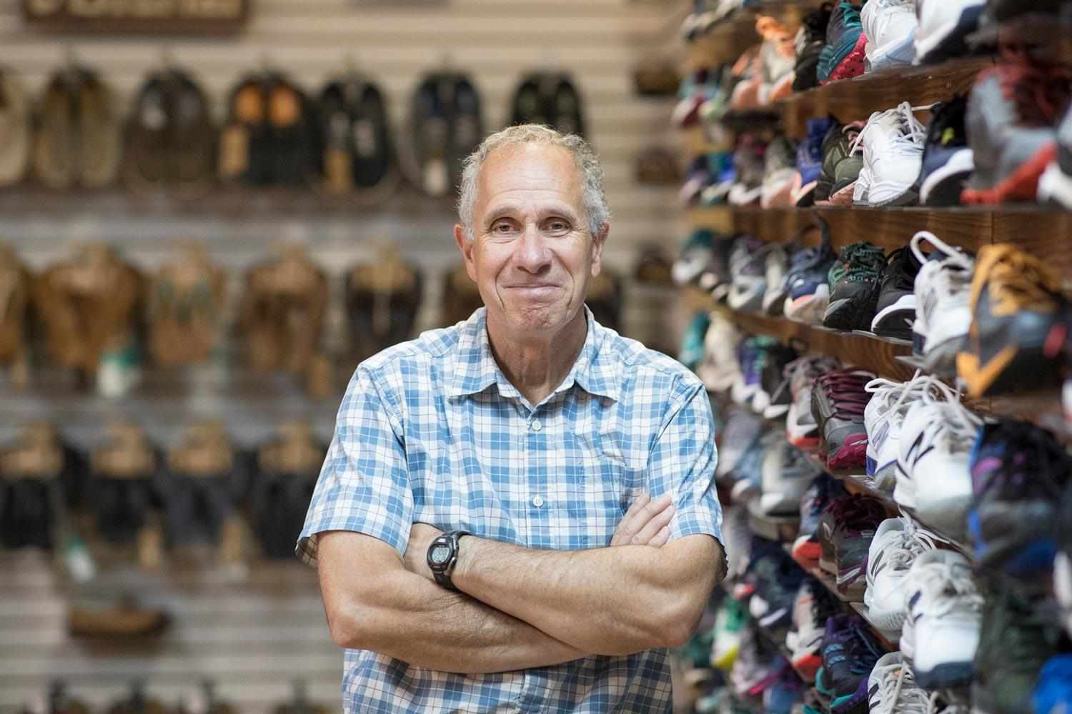 Mark Lorenzoni stands with arms crossed next to a wall full of shoes