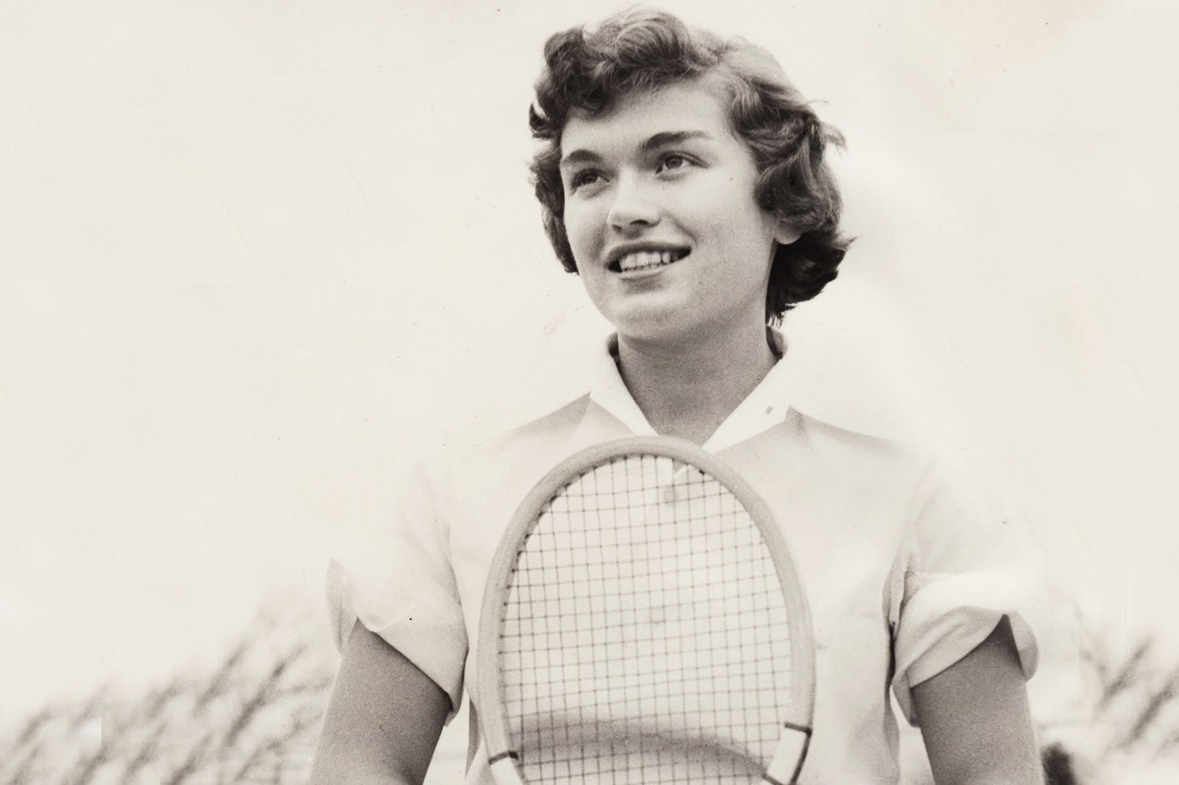 black and white photo of Slaughter standing with a tennis racket looking to the left of the photo