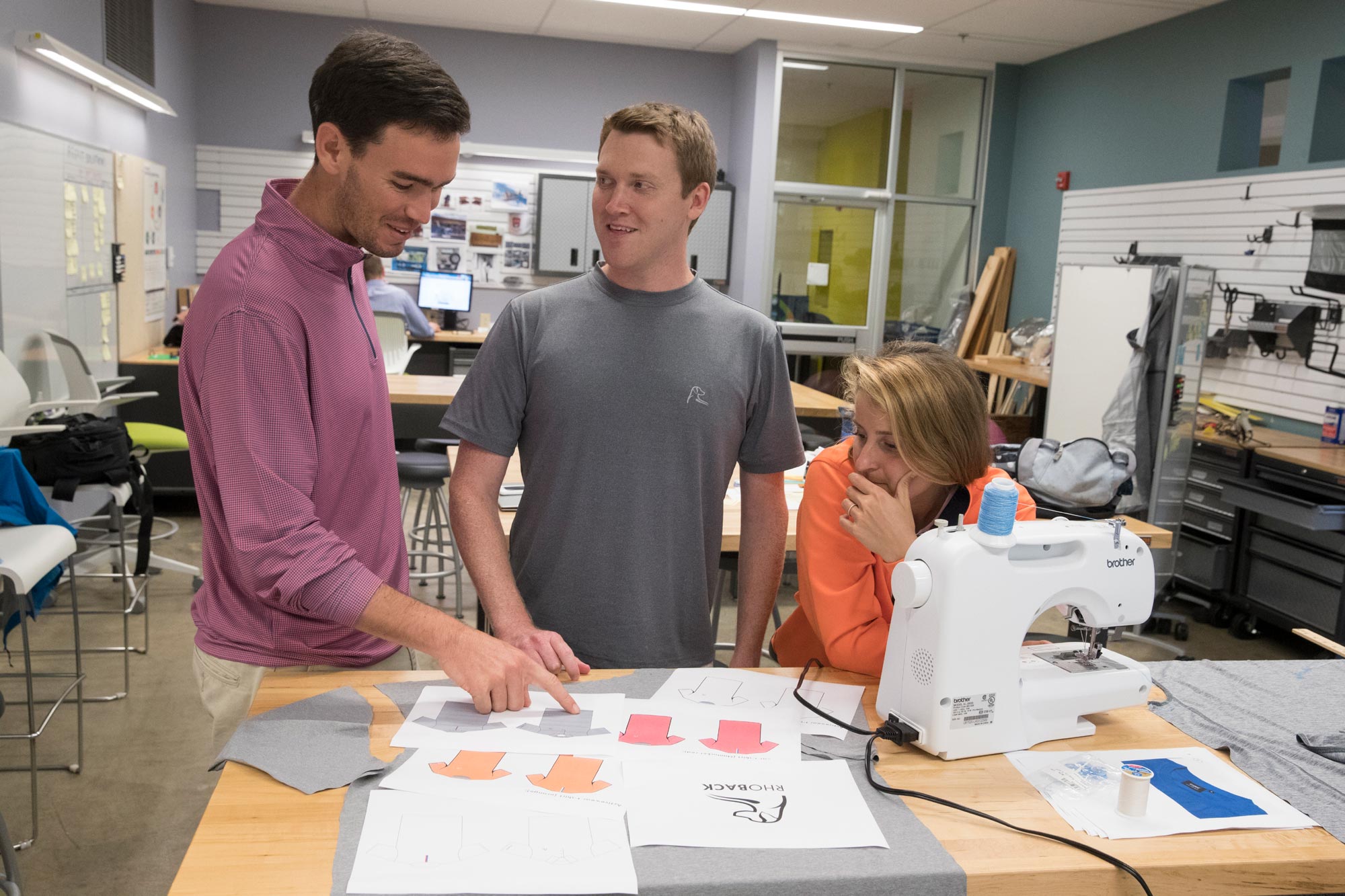Matt Loftus, left, business partner Kevin Hubbard,middle, and Kristina Loftus, right, stand at a table looking at shirt designs