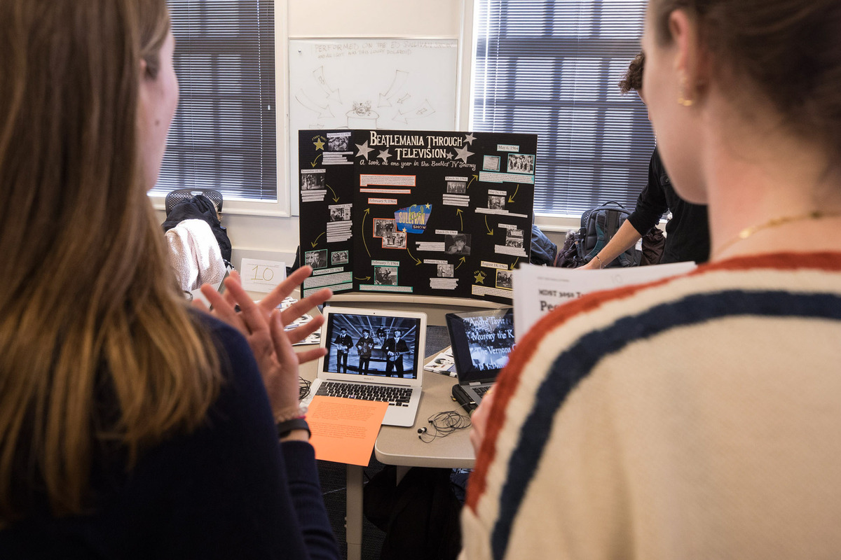 Students stand to look at a tri-fold and computer monitors of old bands playing on them