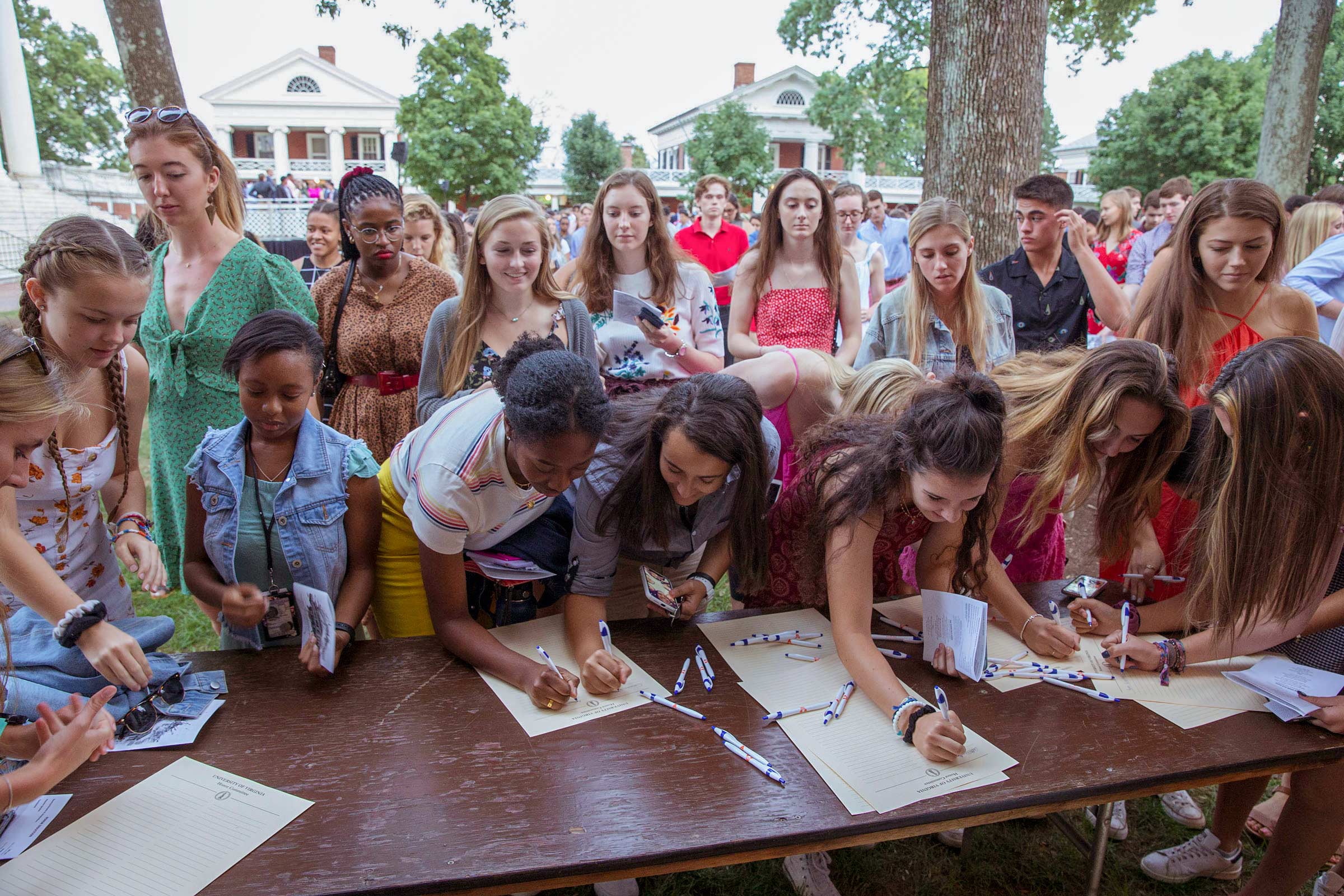 People stand in line as a table full of new students sign the honor code on the Lawn