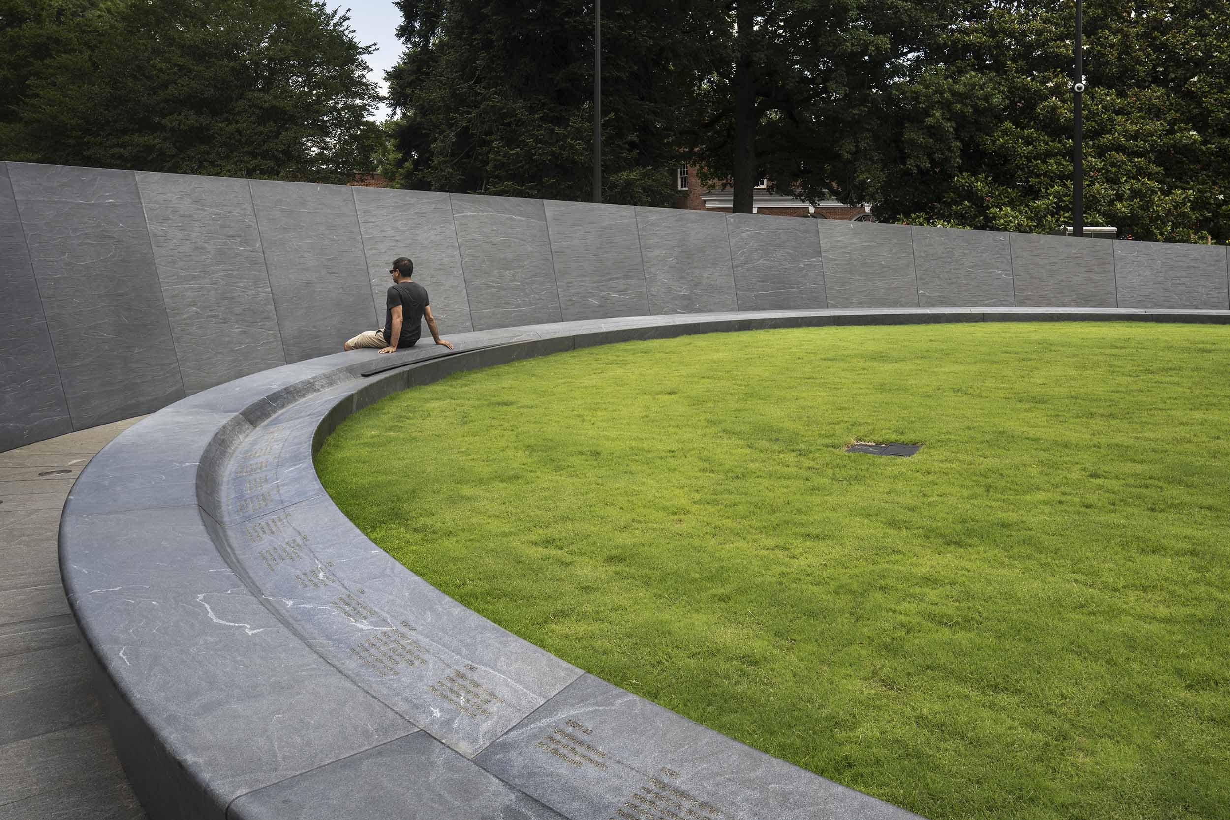 Person sits on the wall of the Memorial for enslaved laborers