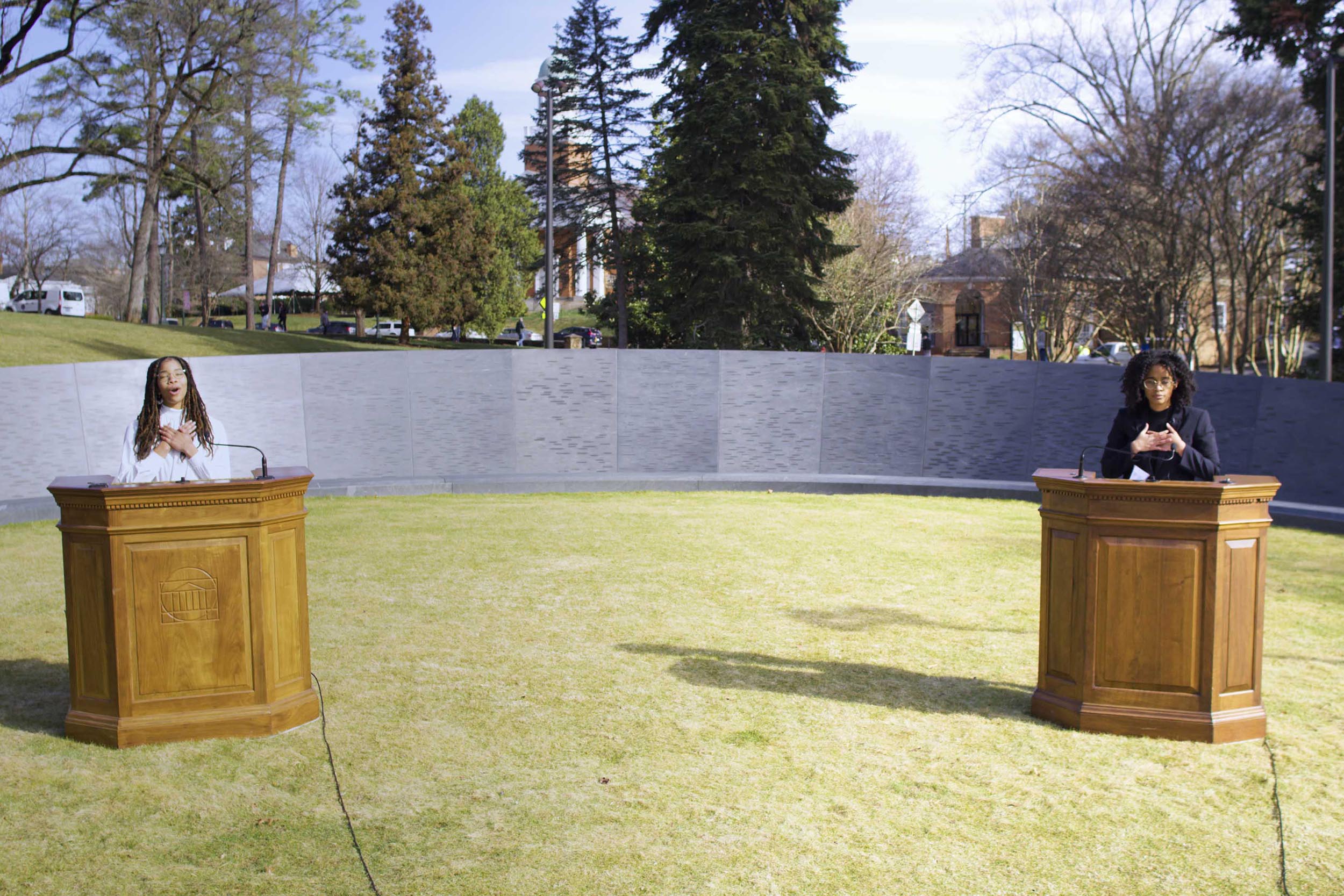 Jayla Hart and Salem Zelalem speak at podiums at the memorial for Enslaved Laborers