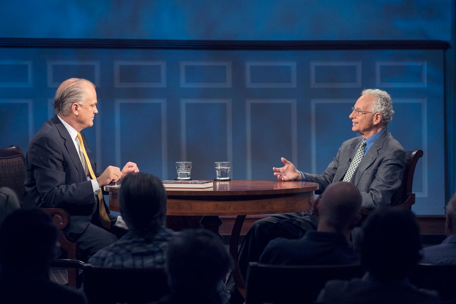 Two people sitting on stage at a round table talking 