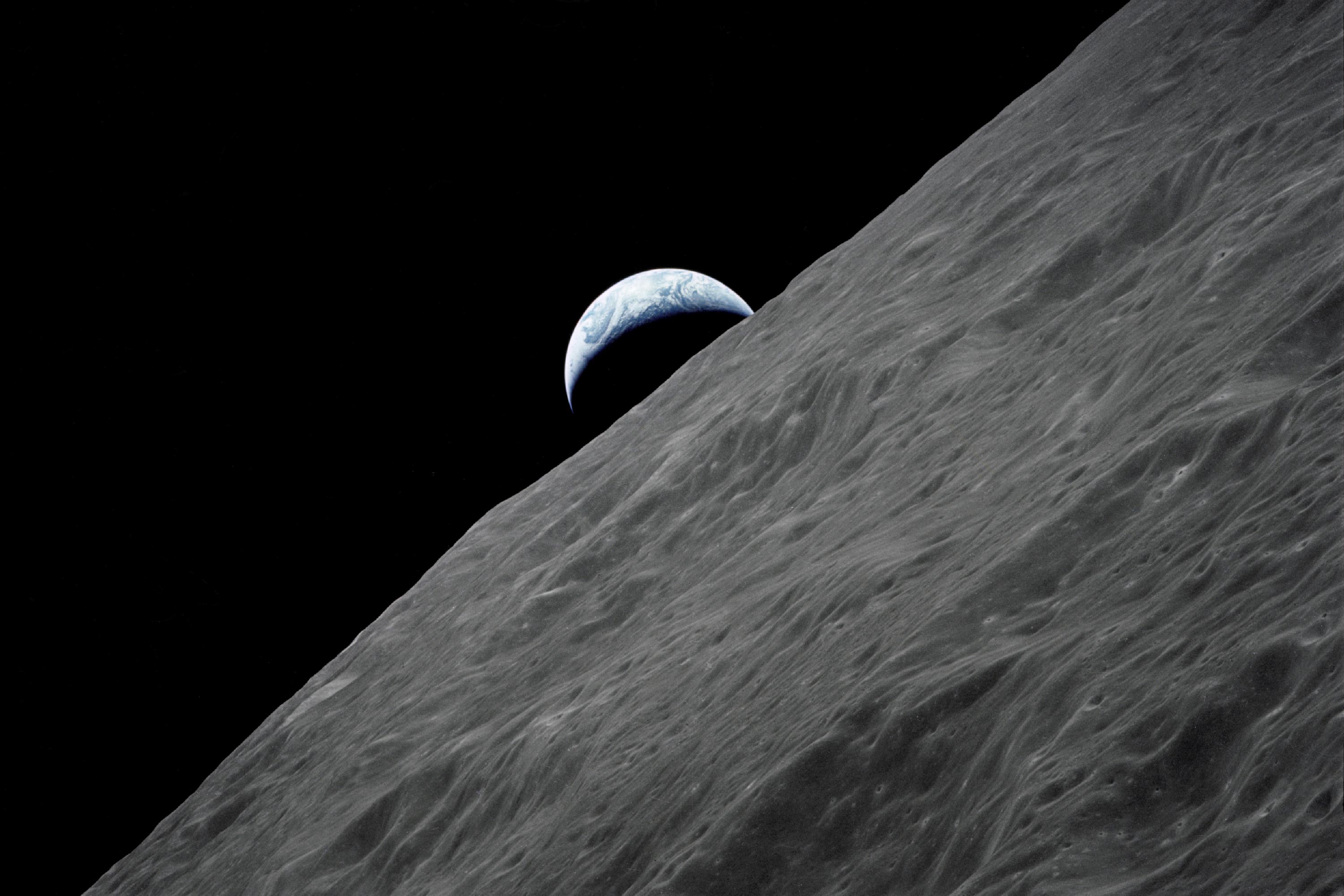 A crescent Earth is seen over the horizon of the moon 